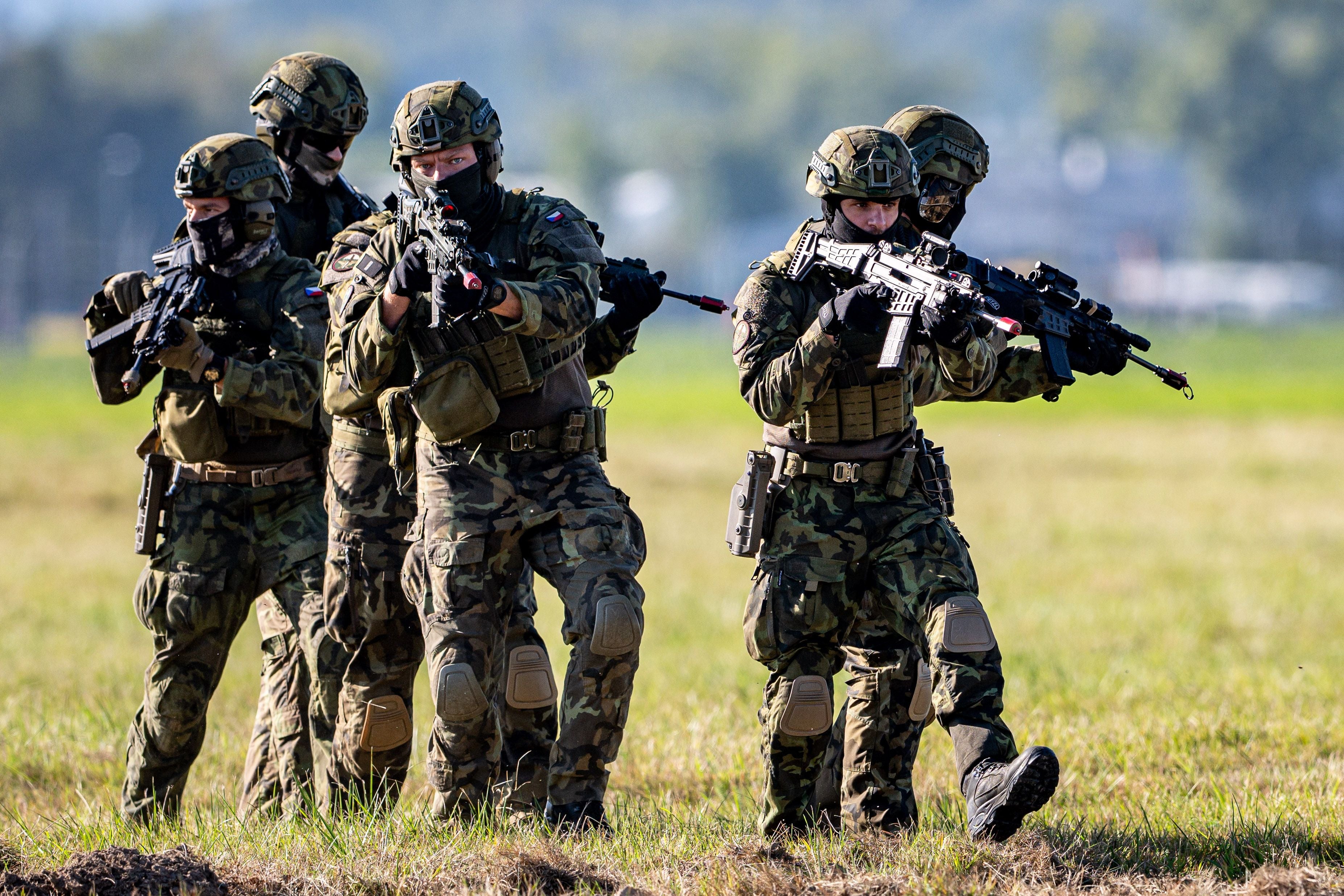 Fünf Soldaten in Tarnuniformen marschieren bewaffnet über eine Wiese bei einer Militärübung.