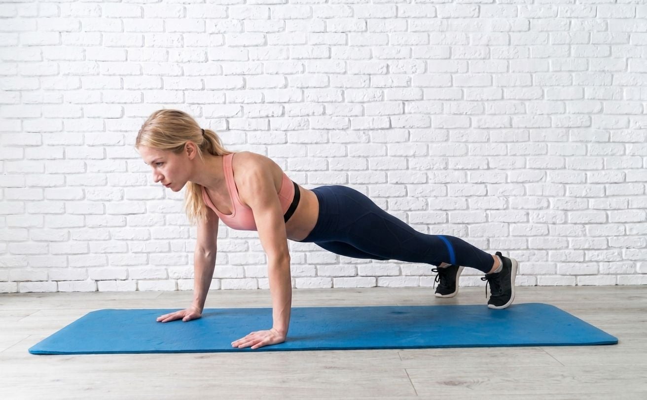 Frau macht Liegestütz auf blauer Fitnessmatte vor weißer Backsteinwand.