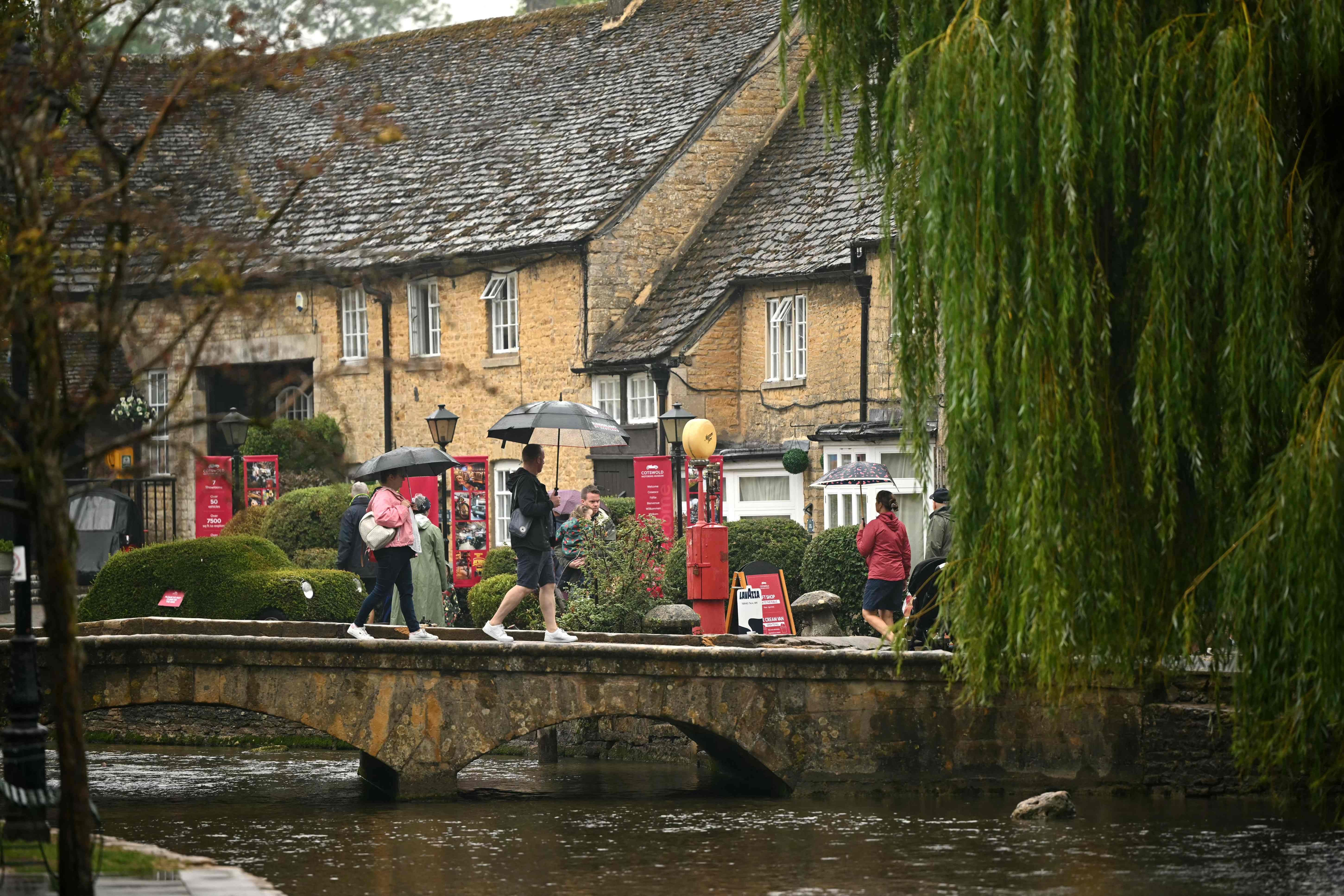 Menschen mit Regenschirmen überqueren eine Steinbrücke vor alten Häusern im regnerischen Bourton-on-the-Water.