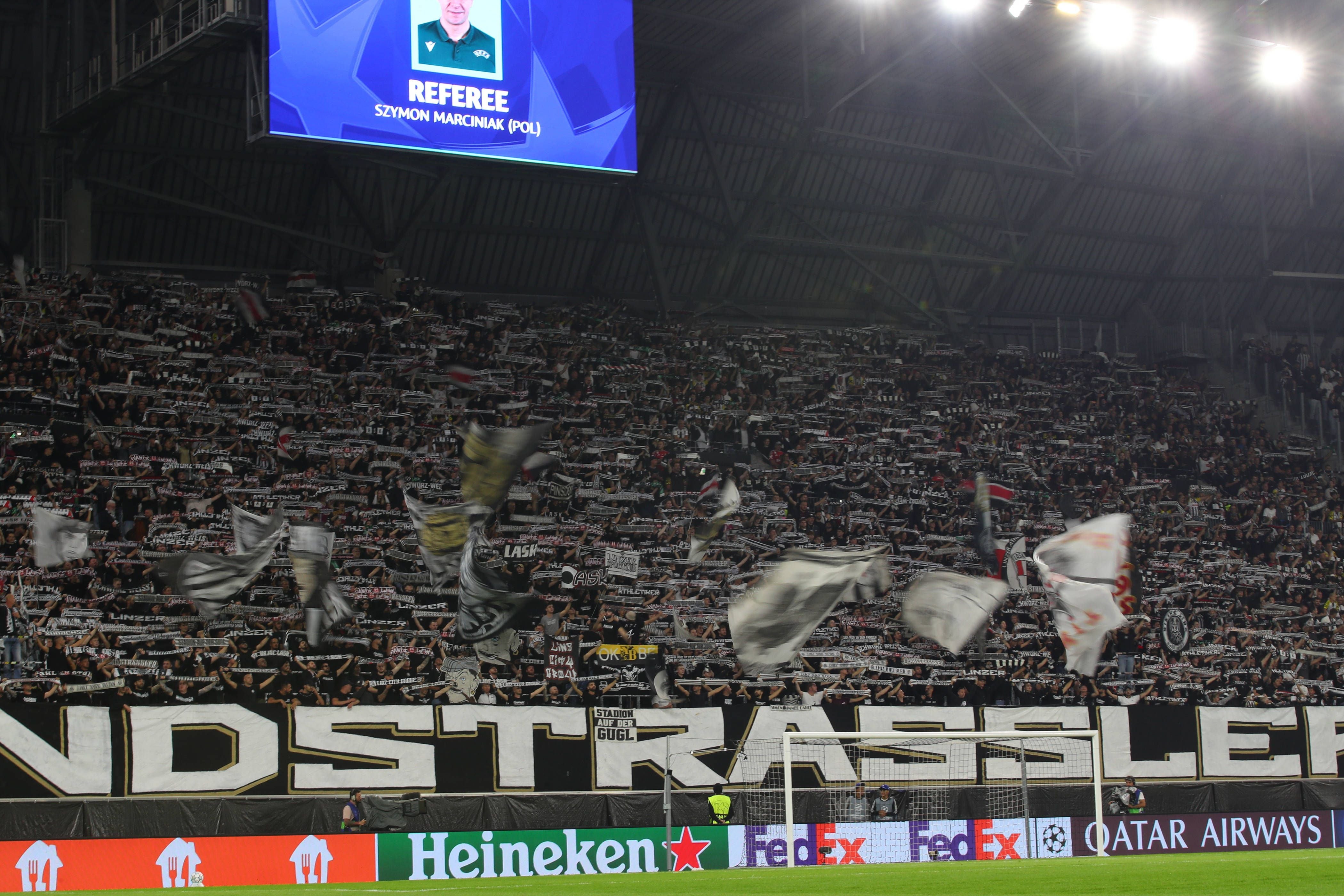 Fans von LASK schwenken Fahnen und Schals im vollen Stadion bei einem Fußballspiel.