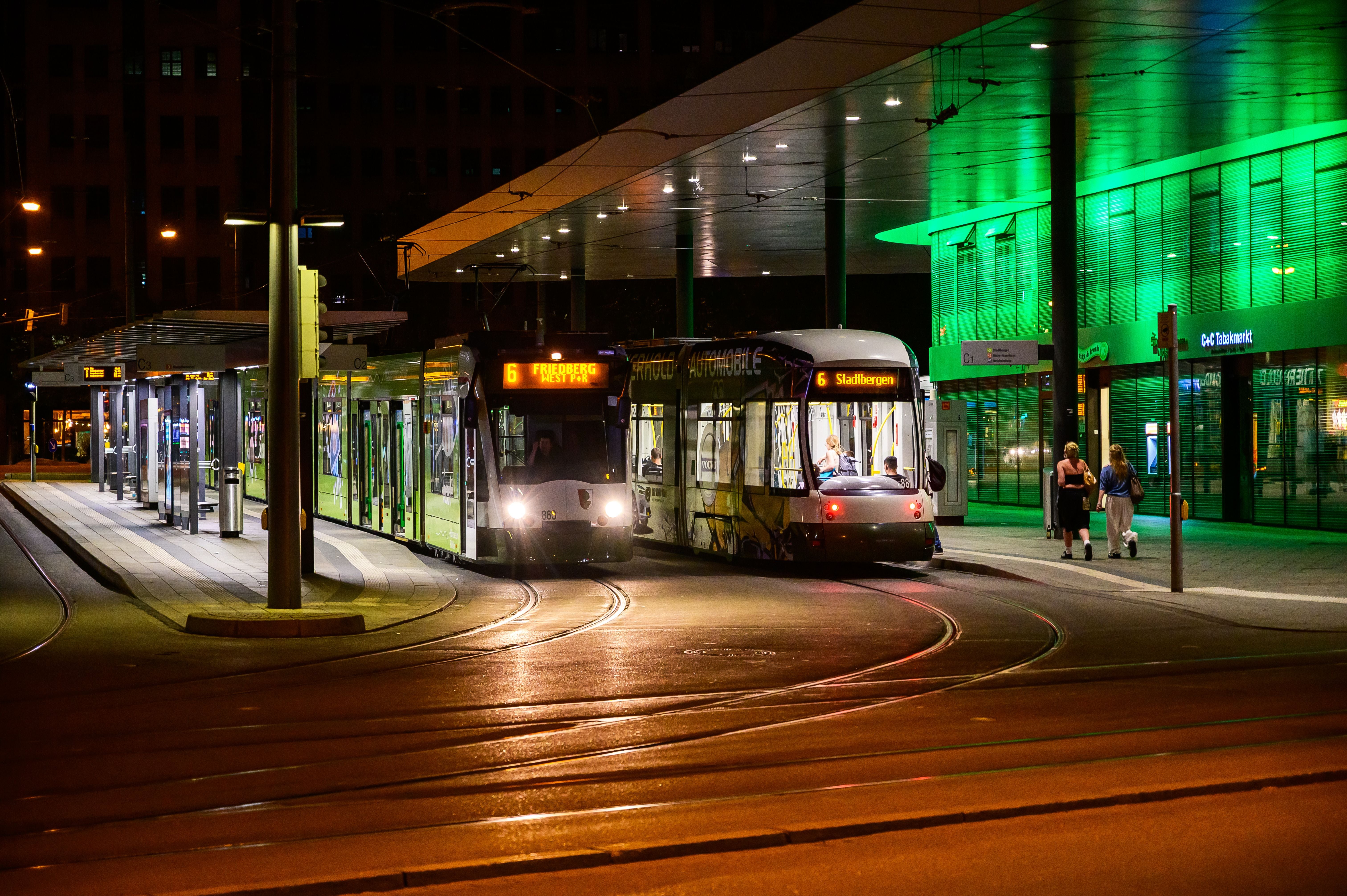 Zwei moderne Straßenbahnen an einem beleuchteten Bahnsteig in Augsburg bei Nacht.