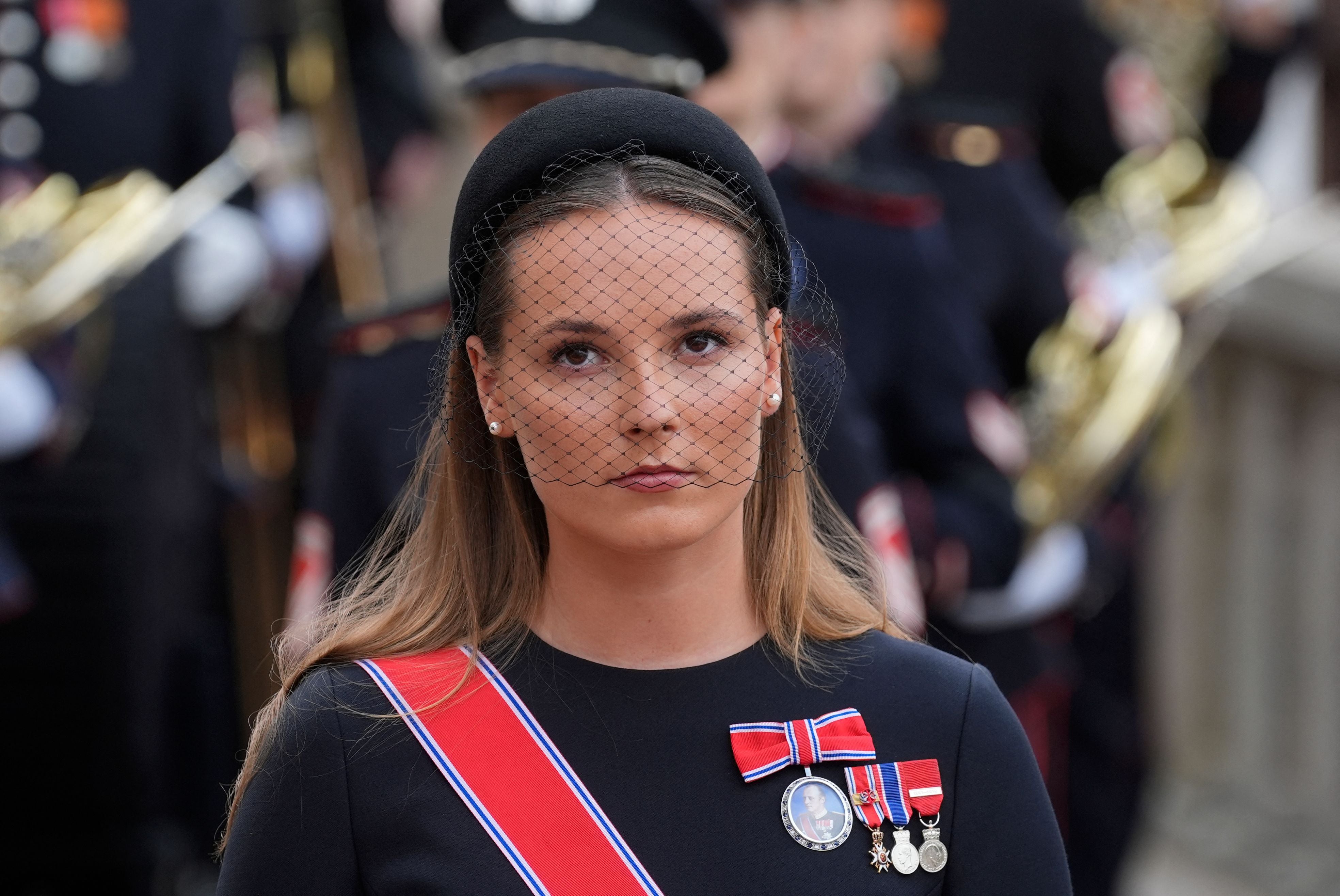 Eine Frau mit Schleierhut und Medaillen trägt eine schwarze Kleidung bei einer Zeremonie.