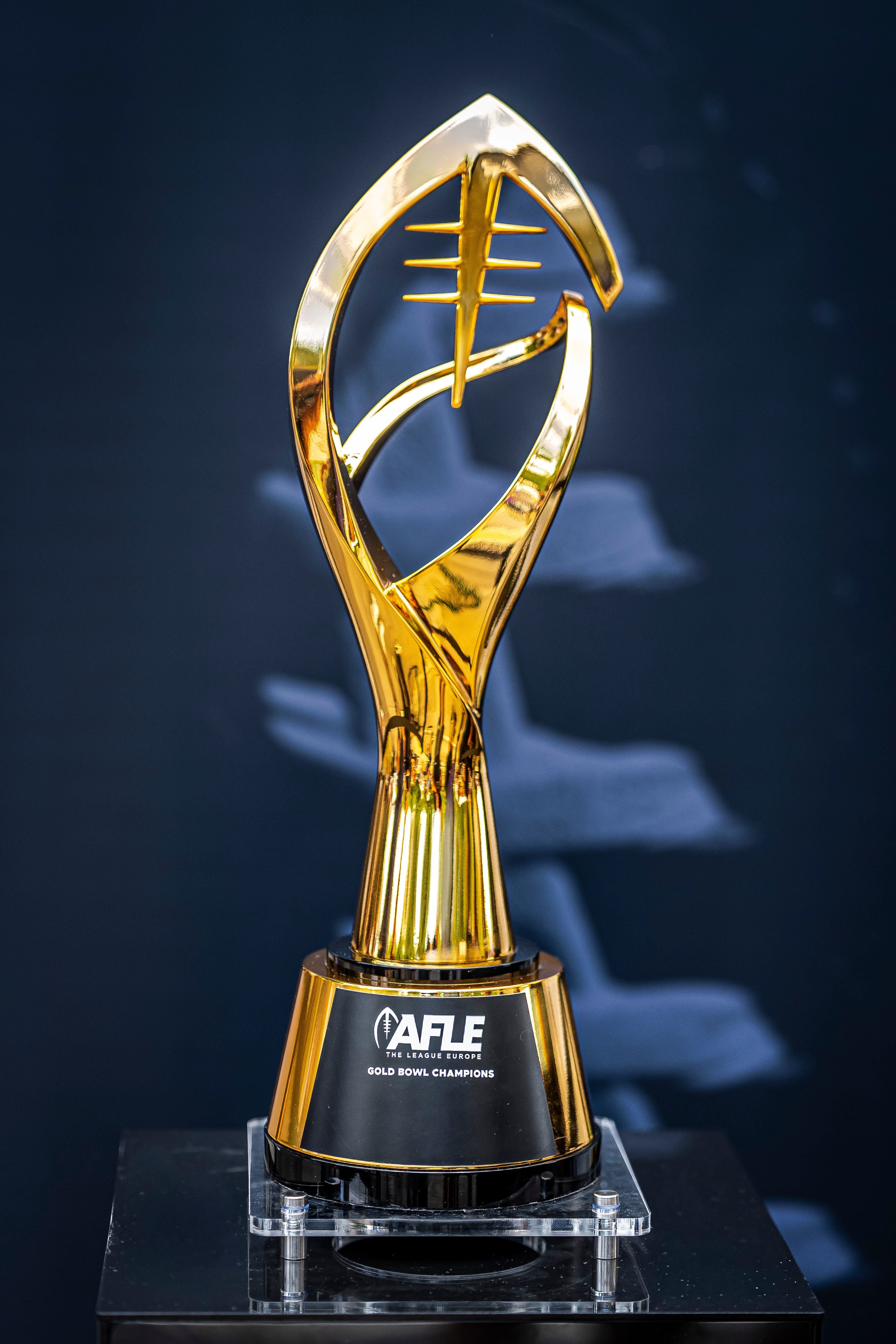 Goldene Trophäe der AFLE Gold Bowl Champions auf dunklem Hintergrund.
