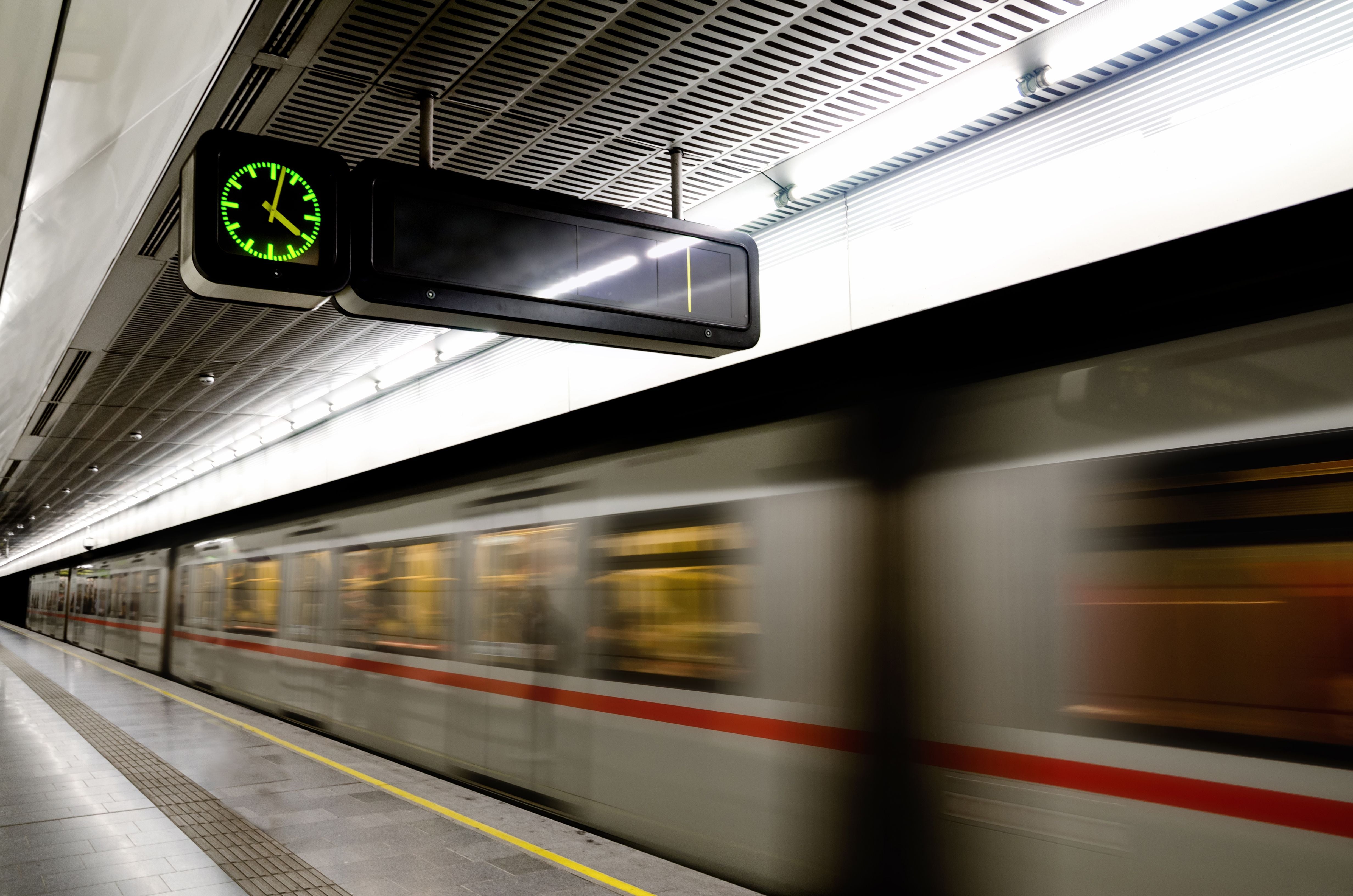 U-Bahn-Station in Wien mit einfahrendem Zug und digitaler Uhr an der Decke.