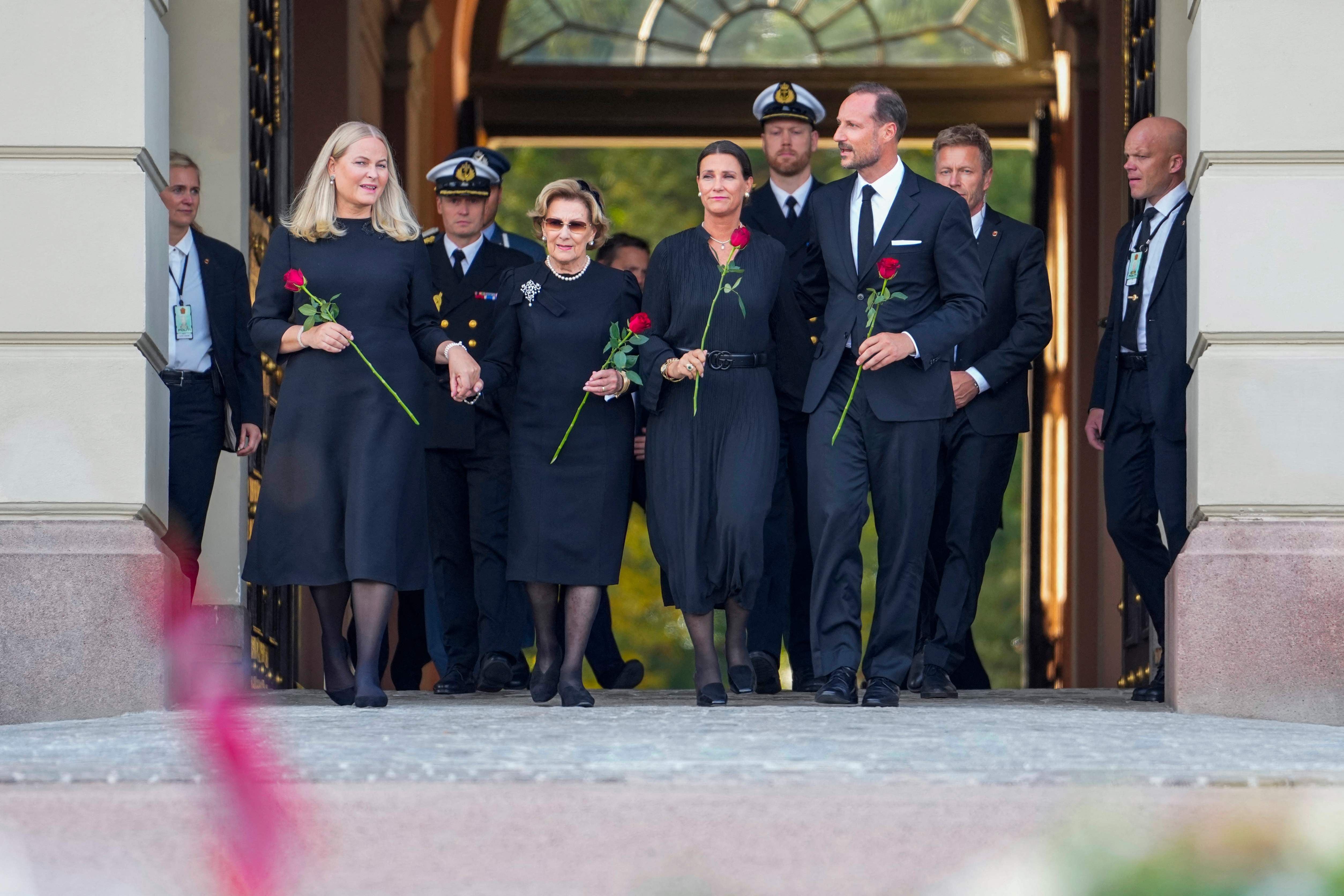 Mehrere Menschen in schwarzer Kleidung halten rote Rosen und gehen aus einem Gebäude.