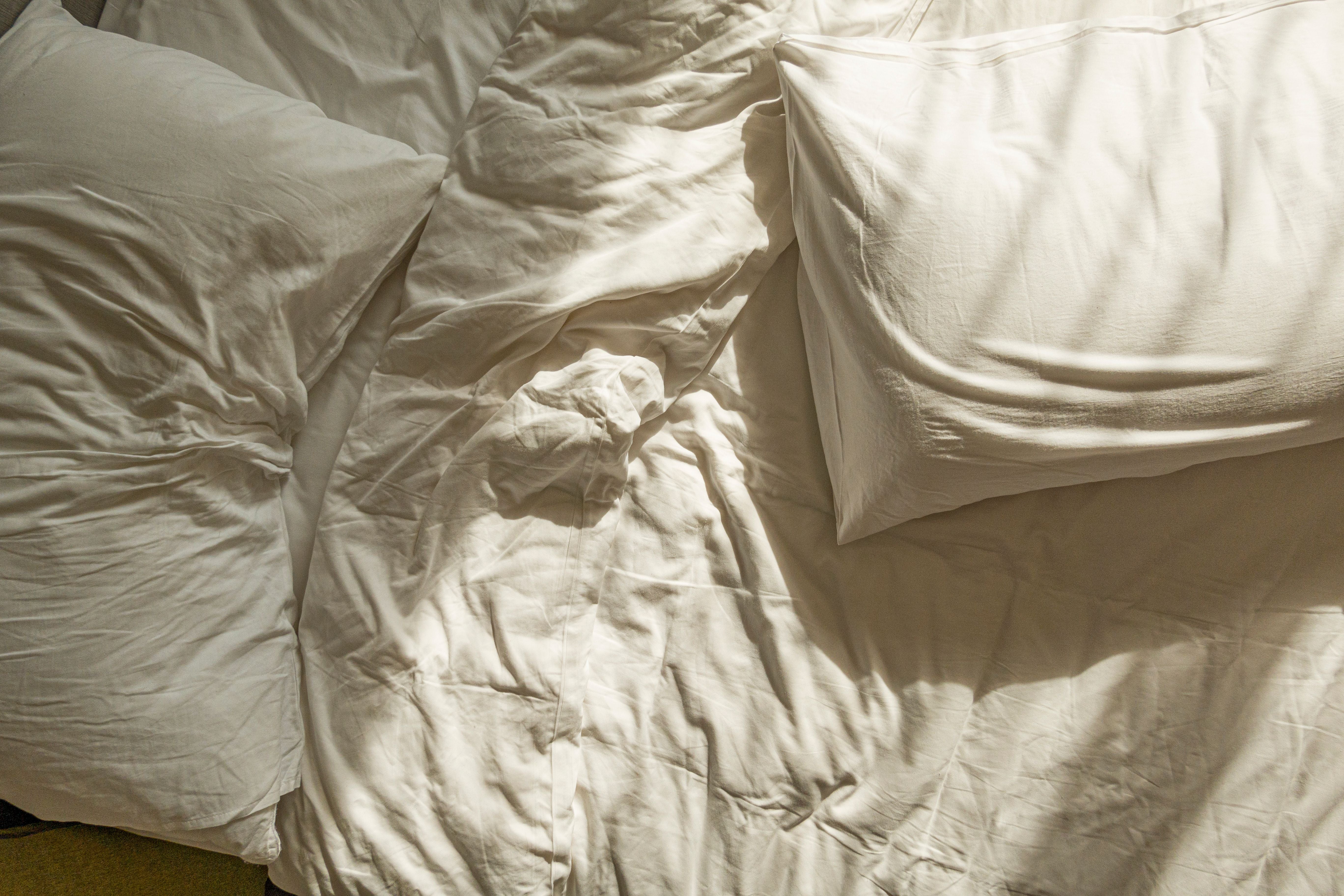 Zwei zerknitterte weiße Kopfkissen auf einem unordentlichen Bett mit weißer Bettwäsche.
