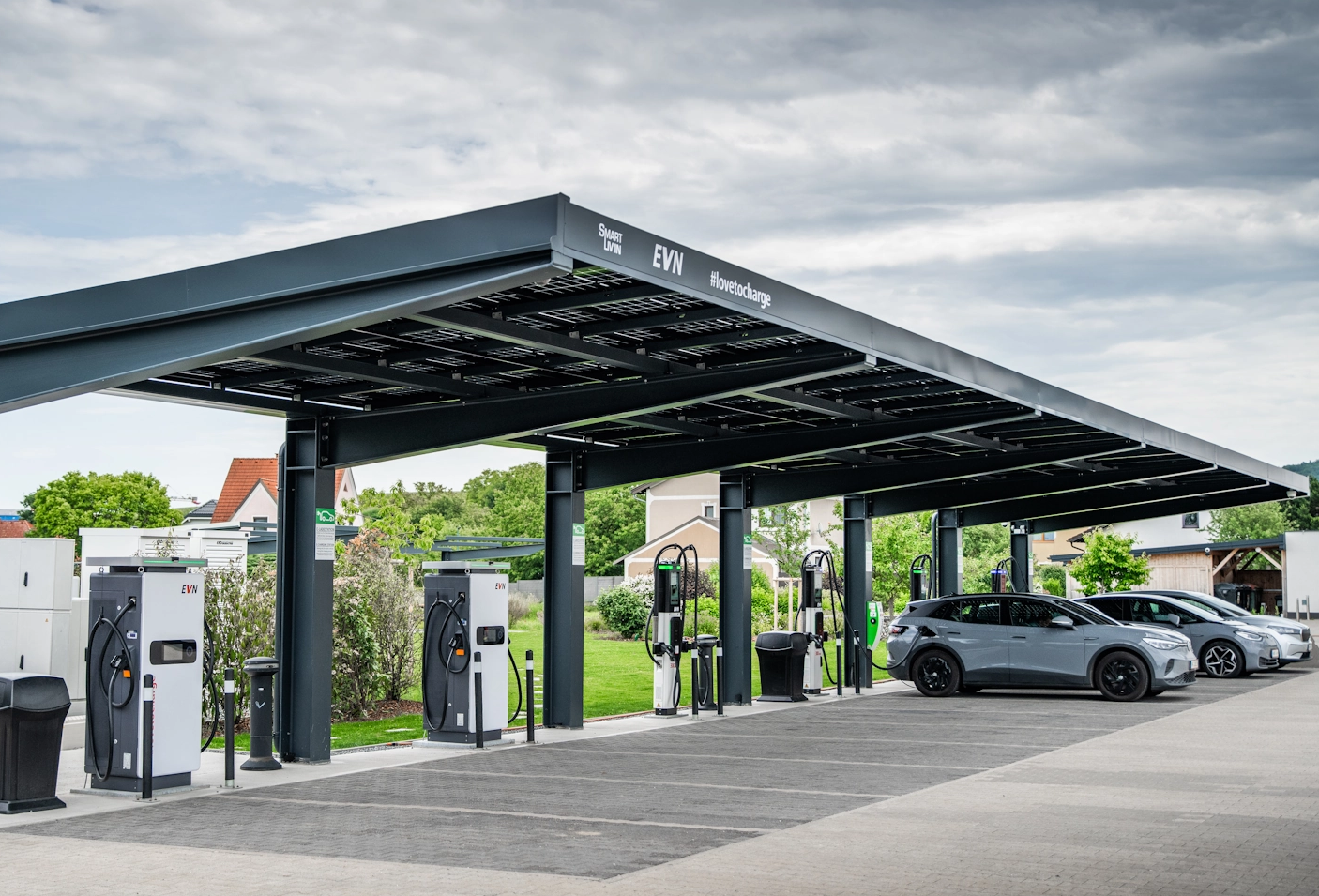 Überdachte Ladestation für Elektroautos mit mehreren Ladesäulen und geparkten Fahrzeugen.