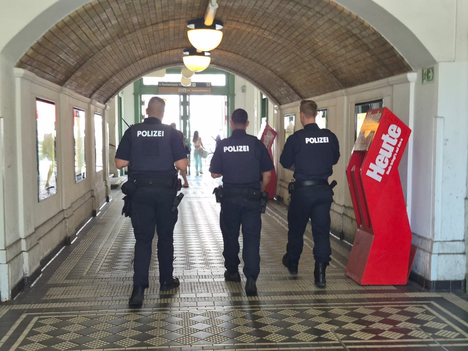 Drei Polizisten gehen durch einen überdachten Gang an der Gumpendorfer Straße.