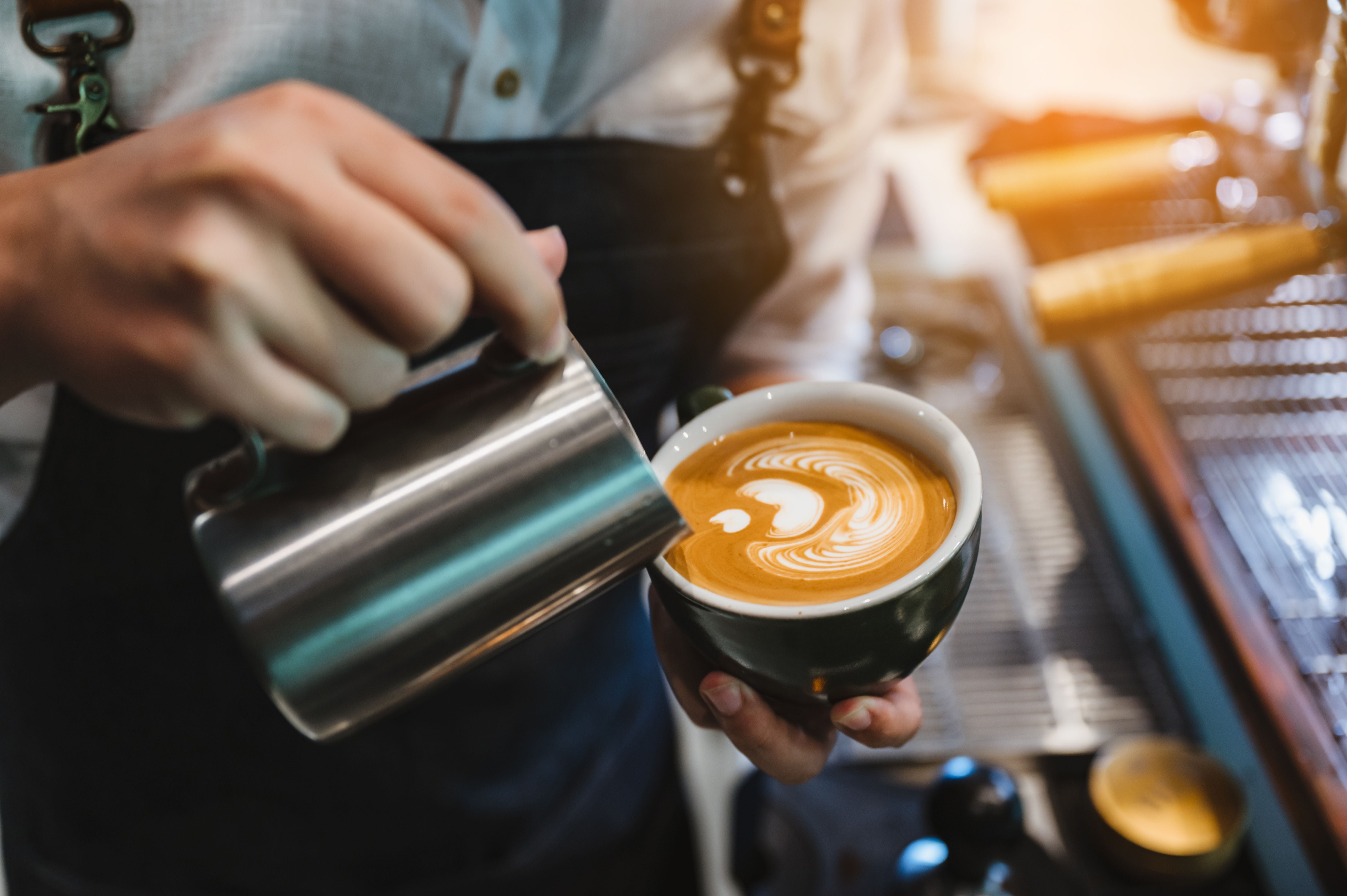 Barista gießt Latte Art in eine Tasse Kaffee, Fokus auf das Muster im Milchschaum.