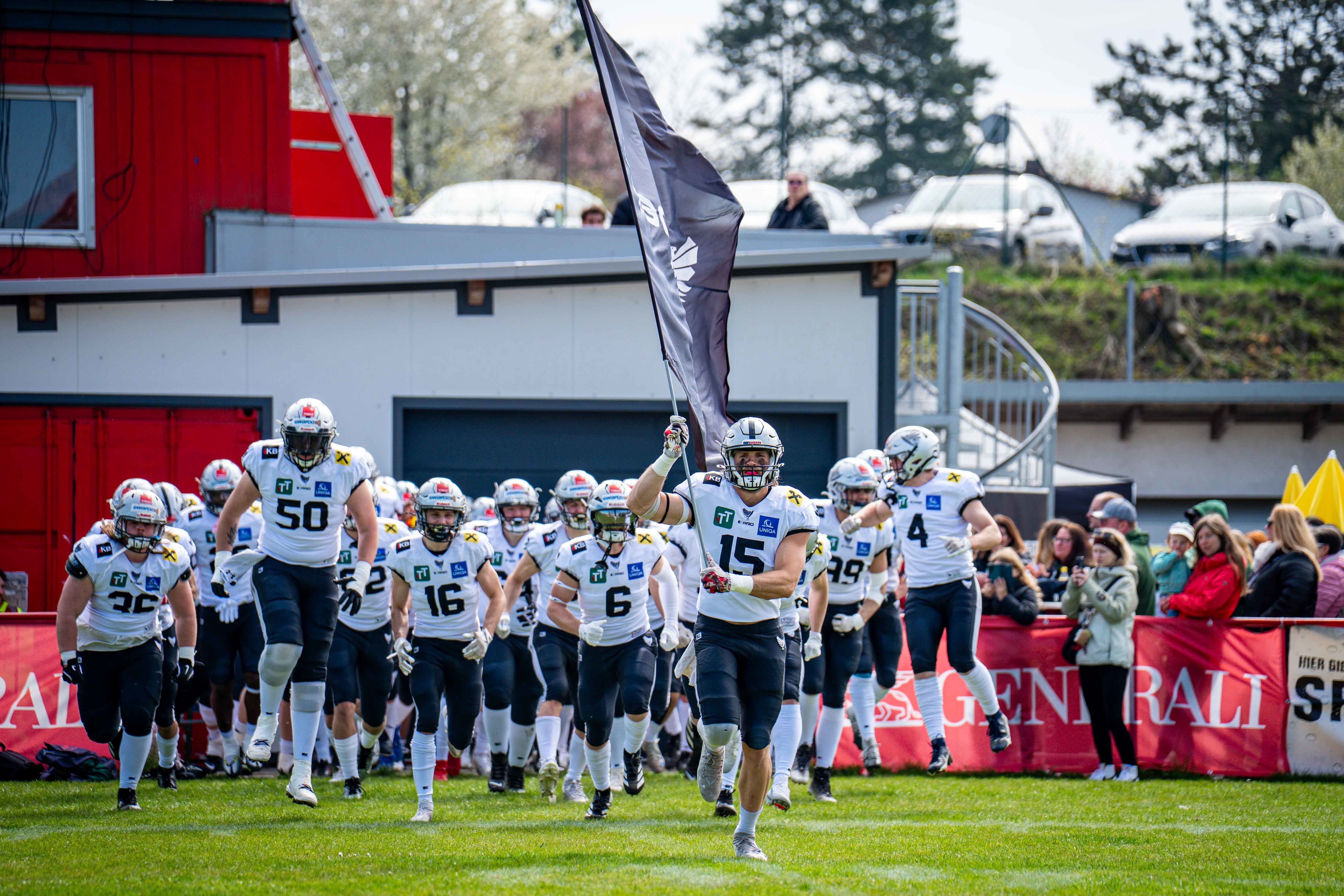 Das Team der Raiders Tirol läuft mit einer Fahne aufs Footballfeld, Zuschauer im Hintergrund.