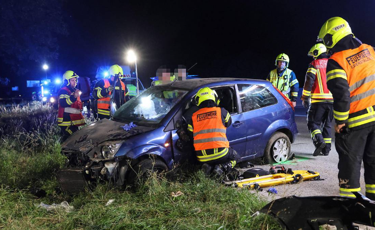 Feuerwehrleute retten nachts nach schwerem Unfall eine Person aus einem stark beschädigten Auto.