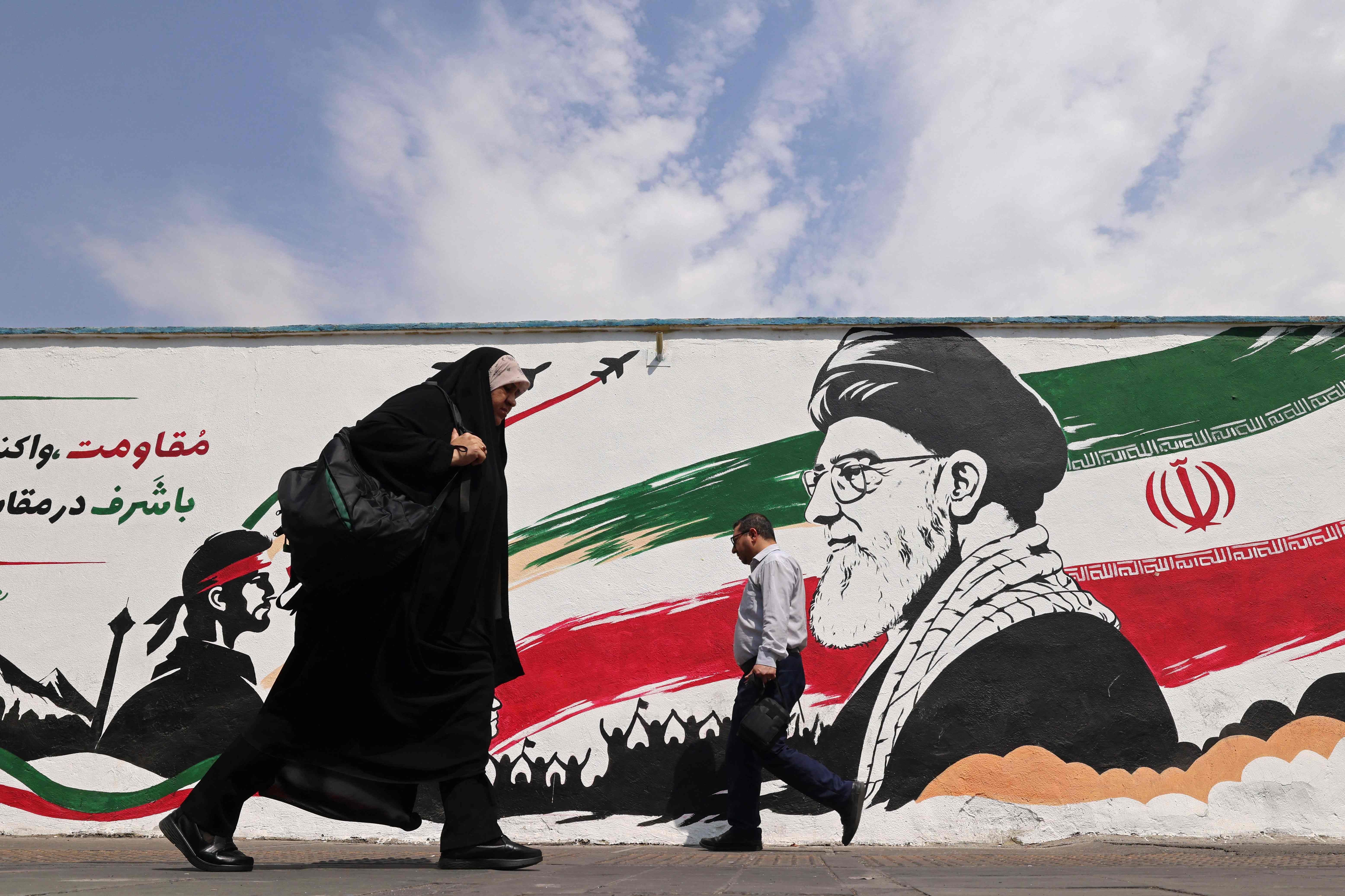 Zwei Passanten gehen an einem Wandgemälde mit Ayatollah Khamenei und iranischer Flagge vorbei.
