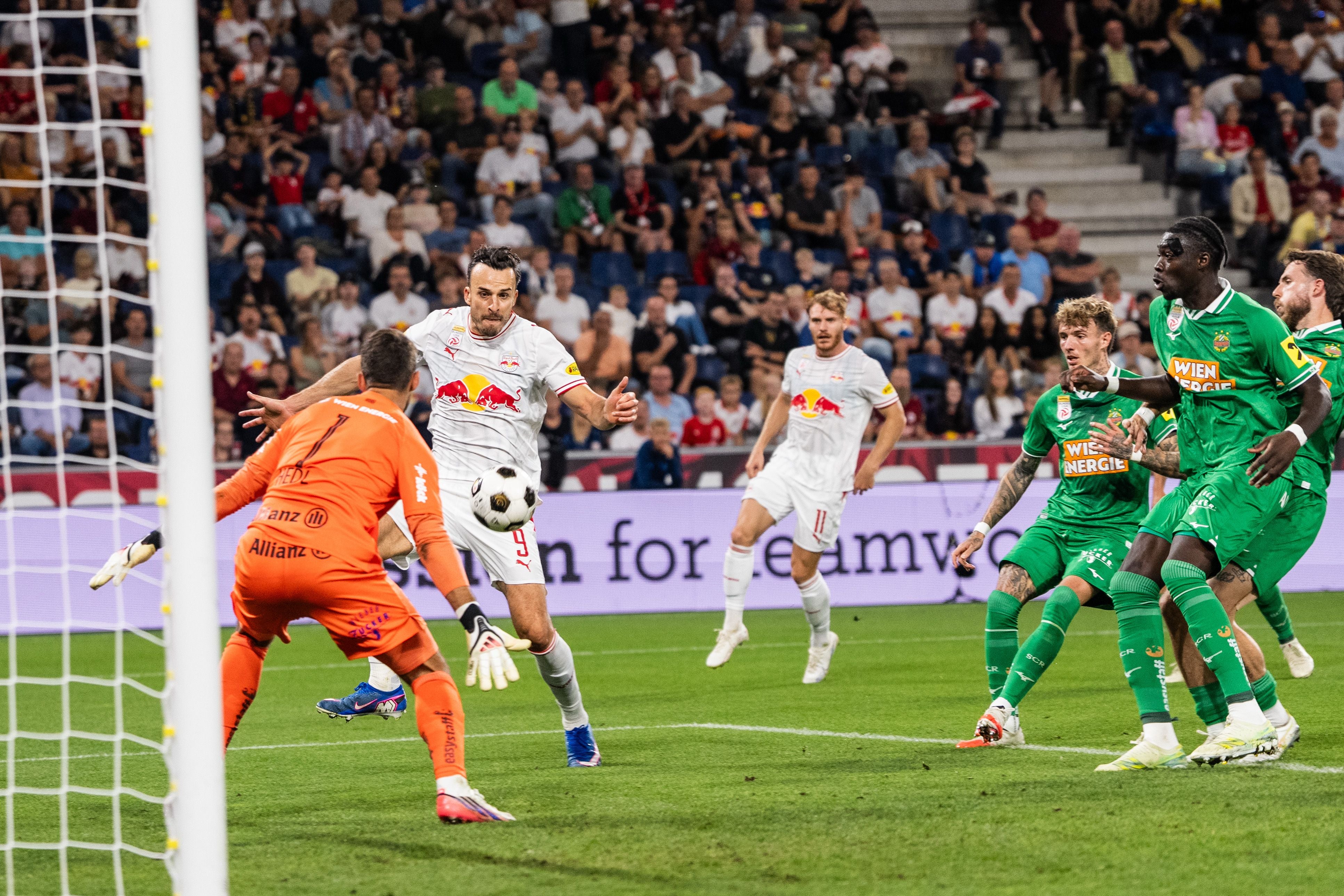 Ein Fußballspieler schießt aufs Tor, während der Torwart und mehrere Gegner versuchen zu blocken.
