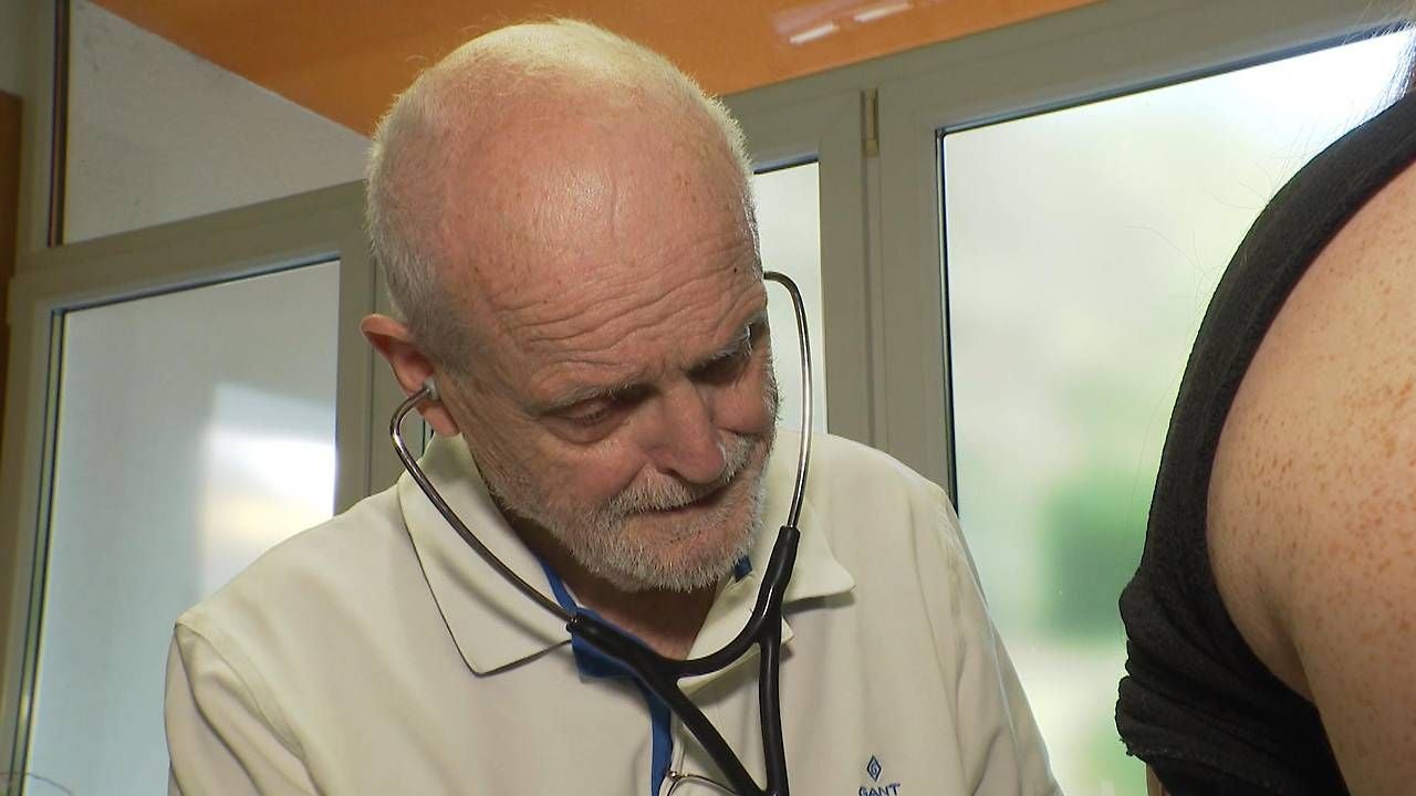 Ein älterer Arzt hört mit einem Stethoskop den Rücken eines Patienten ab.