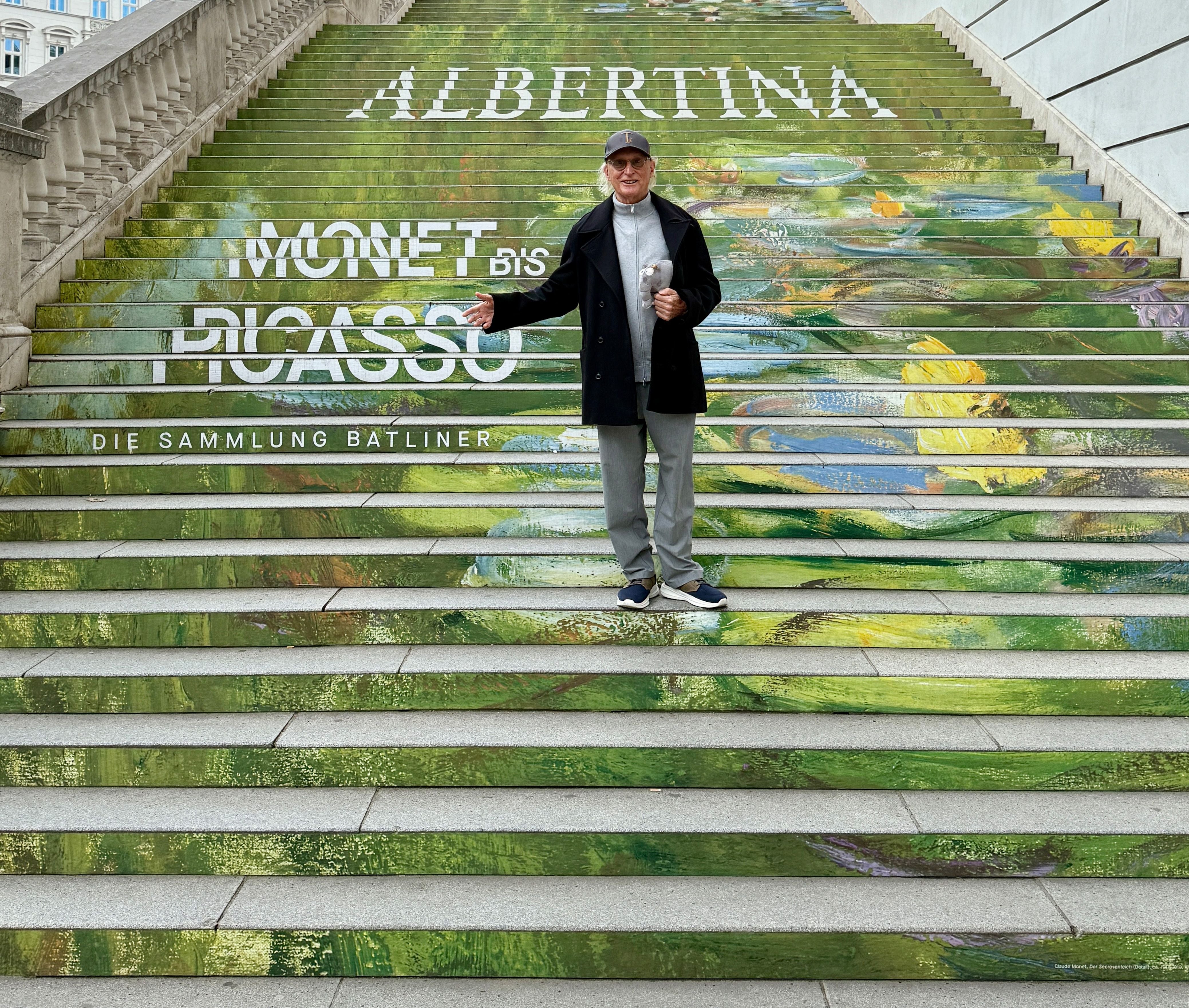Ein Mann steht auf kunstvoll bemalten Stufen mit Schriftzug „ALBERTINA Monet bis Picasso“.