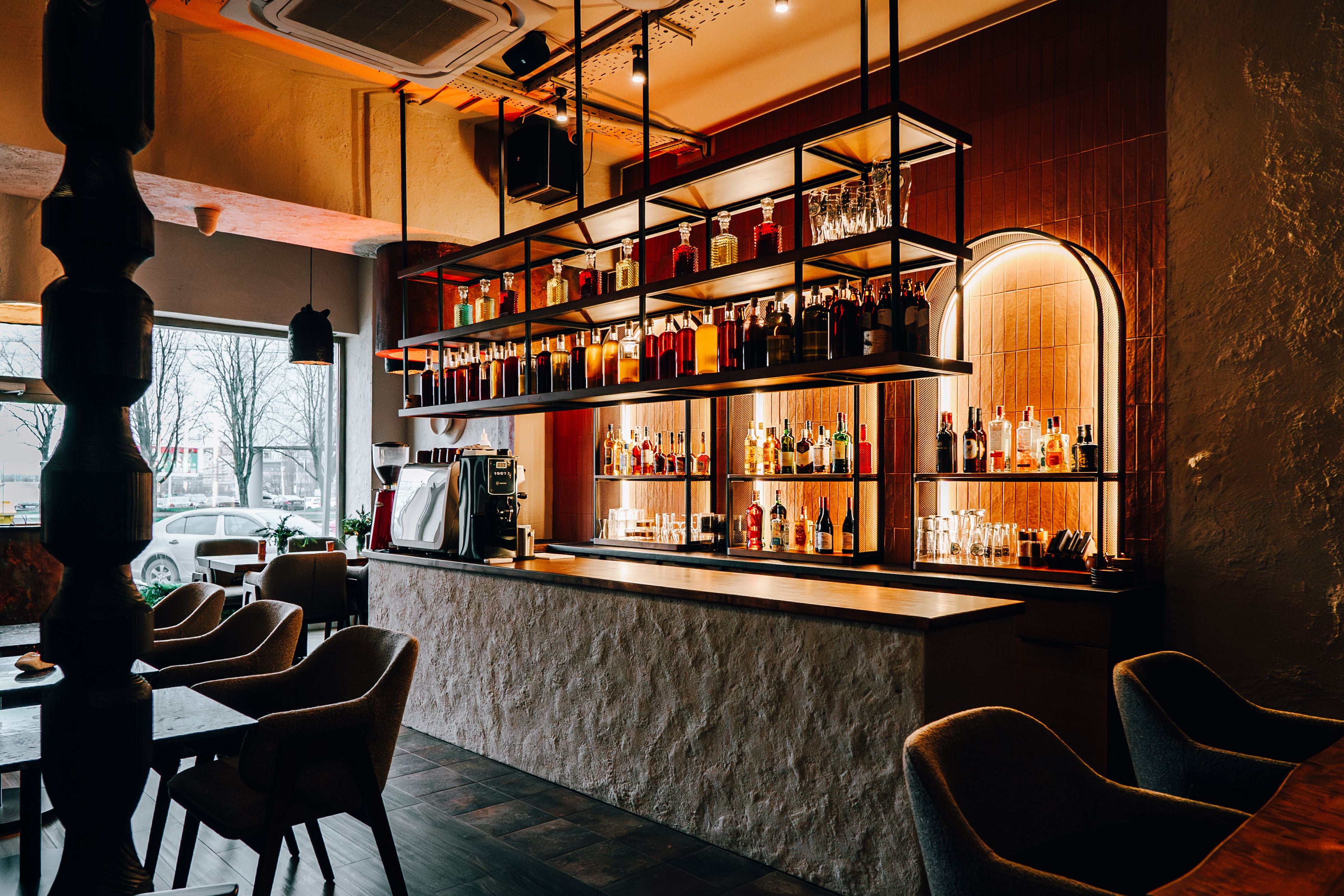 Moderne Bar mit stilvollem Design, warmem Licht und vielen Flaschen Alkohol auf Regalen.