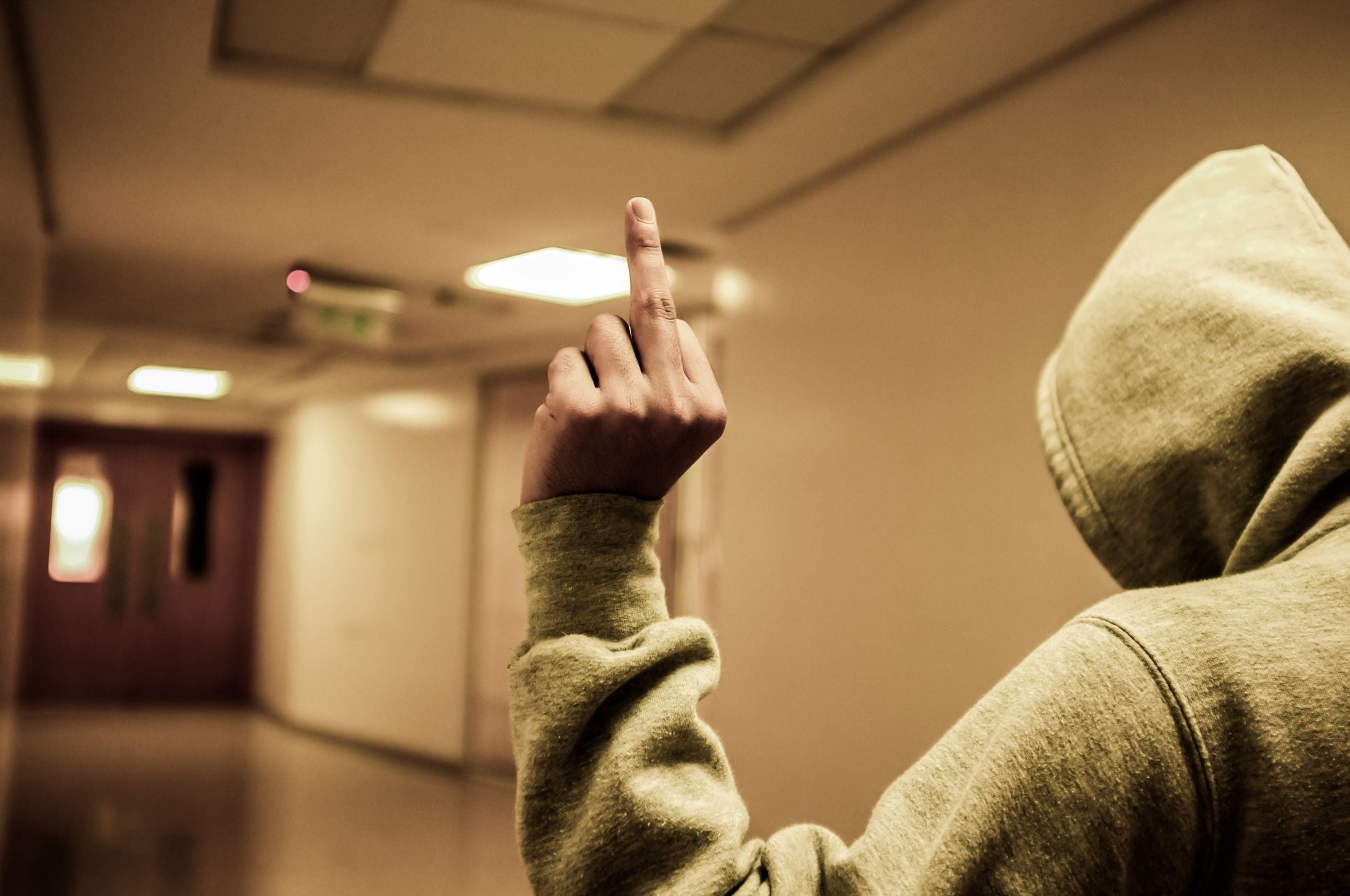 Person in Kapuzenpullover zeigt in einem Flur den Mittelfinger in die Kamera.
