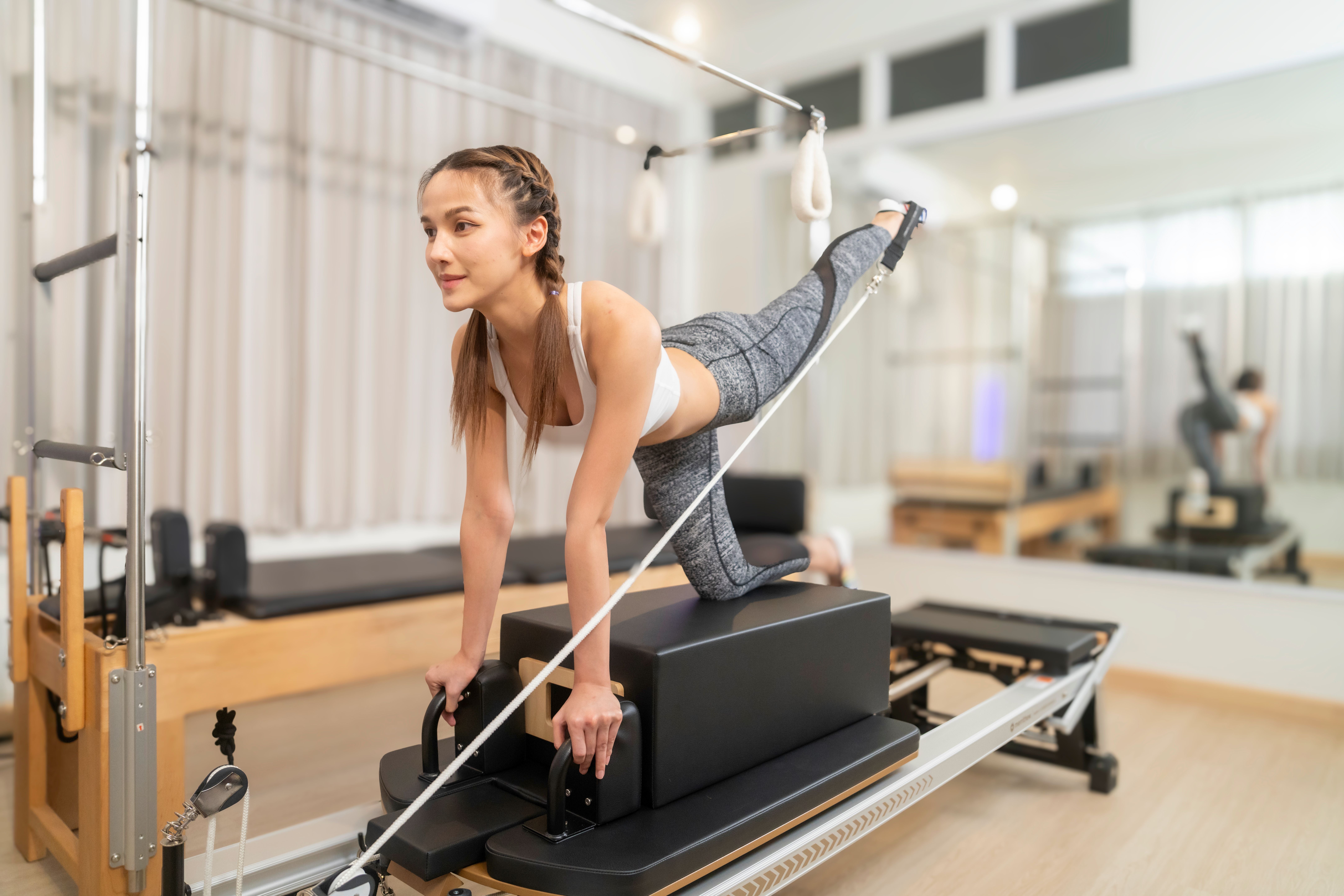 Frau trainiert auf einem Pilates-Reformer-Gerät in einem modernen Fitnessstudio.