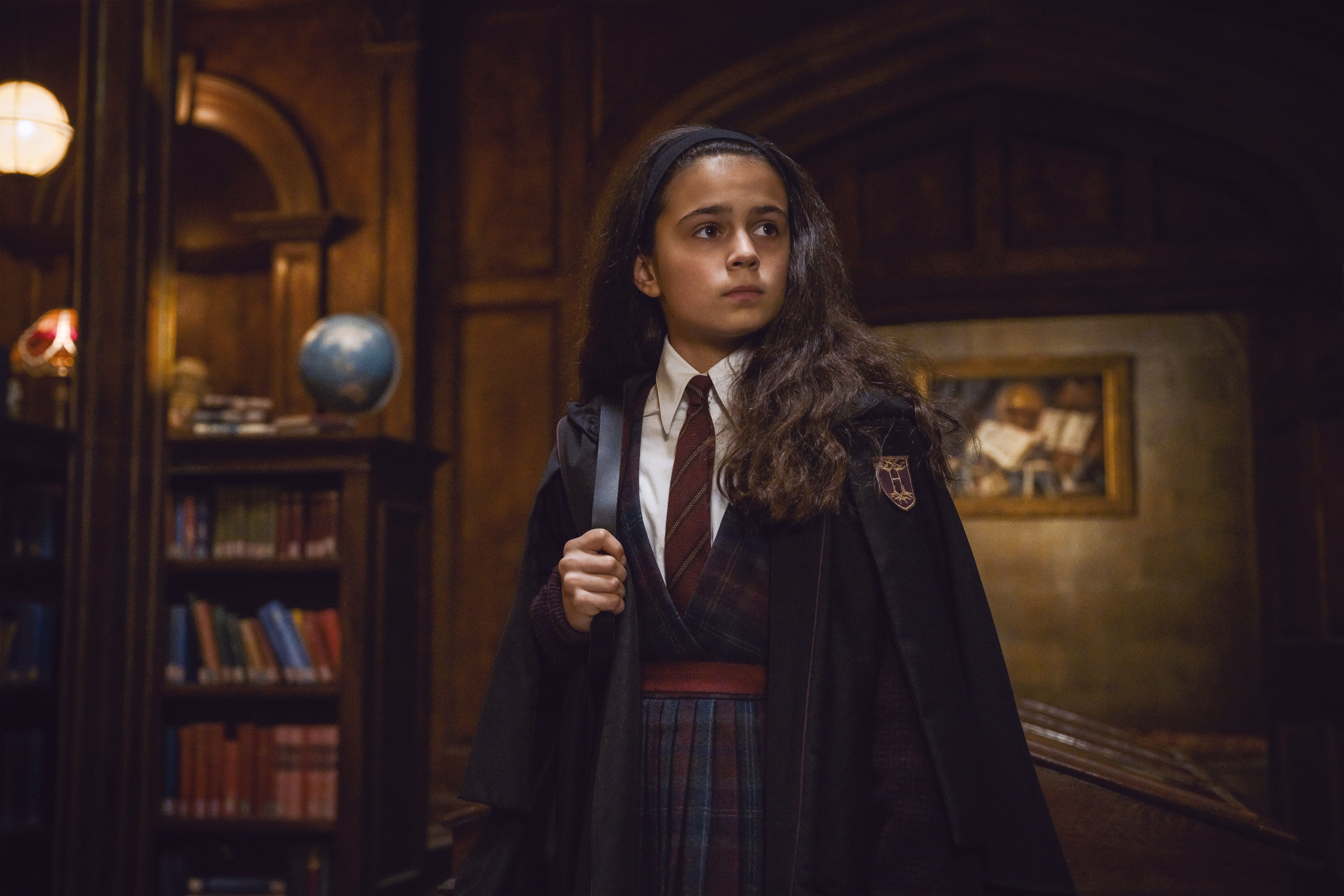 Ein Mädchen in Hogwarts-Schuluniform steht in einer holzgetäfelten Bibliothek.