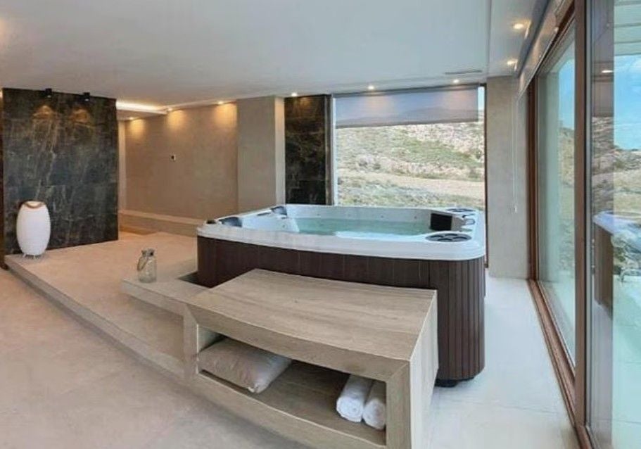 Moderner Raum mit Whirlpool, Holzmöbeln und großen Fenstern mit Blick auf die spanische Landschaft.