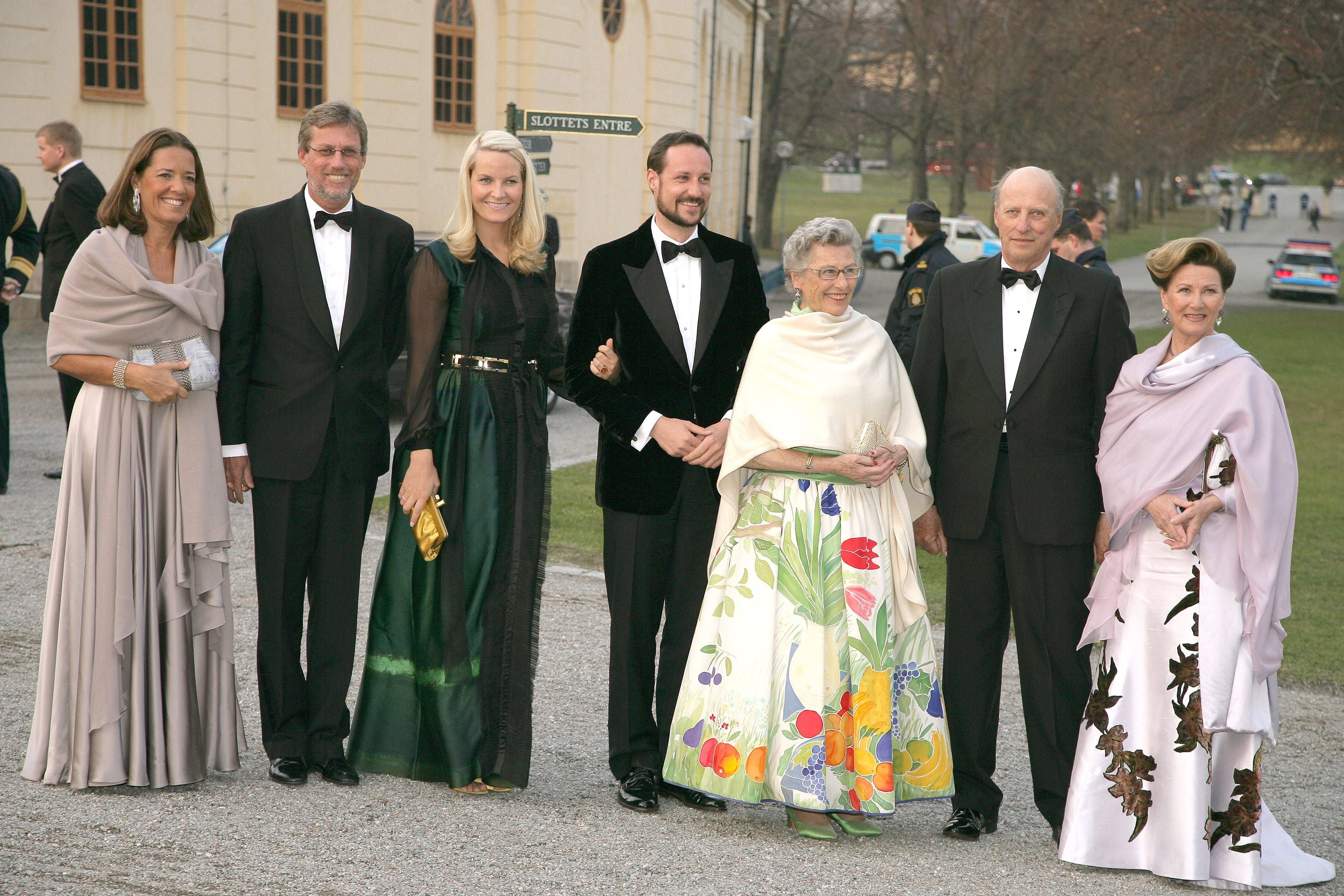 Sieben elegant gekleidete Personen posieren im Freien vor einem historischen Gebäude.