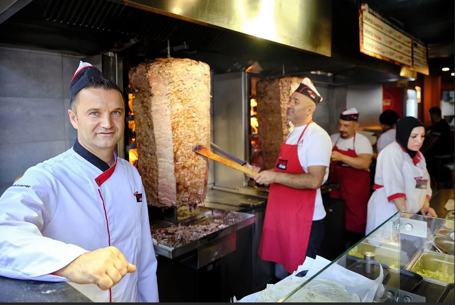 Mehrere Mitarbeiter bereiten Döner in einer Dönerbude mit großen Fleischspießen zu.