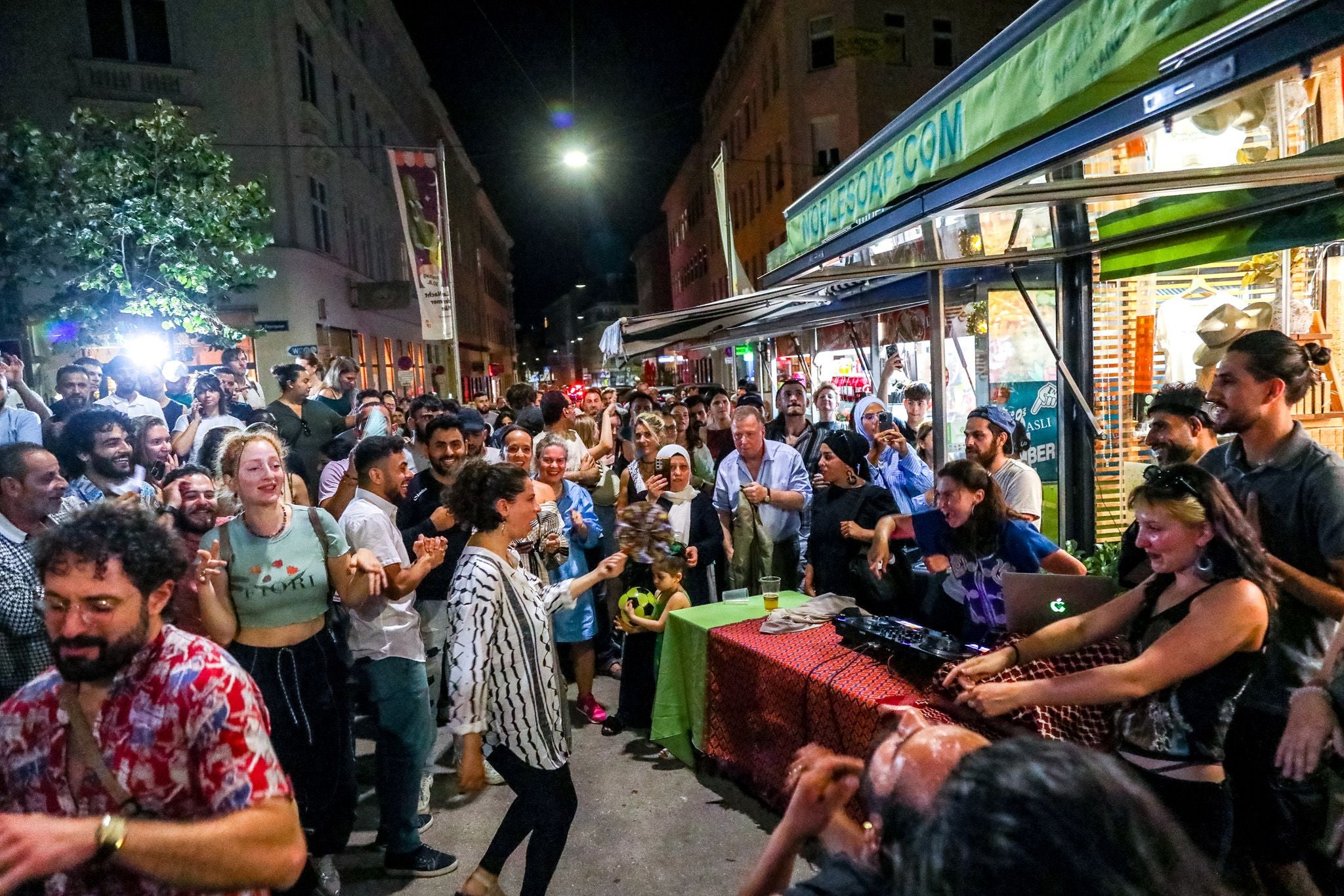 Viele Menschen feiern und tanzen nachts fröhlich auf einem belebten Wiener Markt.