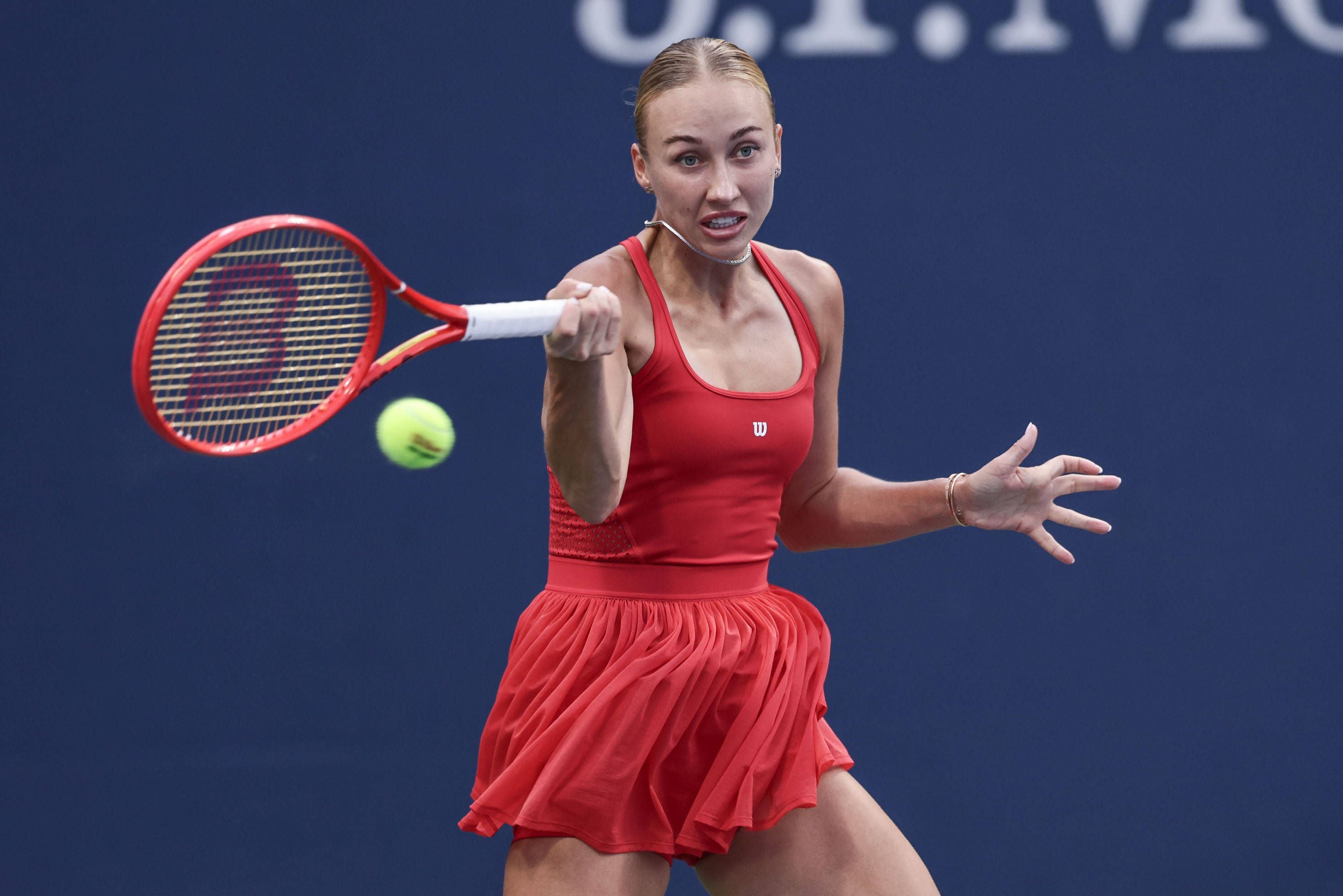 Eine Tennisspielerin in einem roten Top schlägt den gelben Ball mit ihrer Vorhand über den Court.