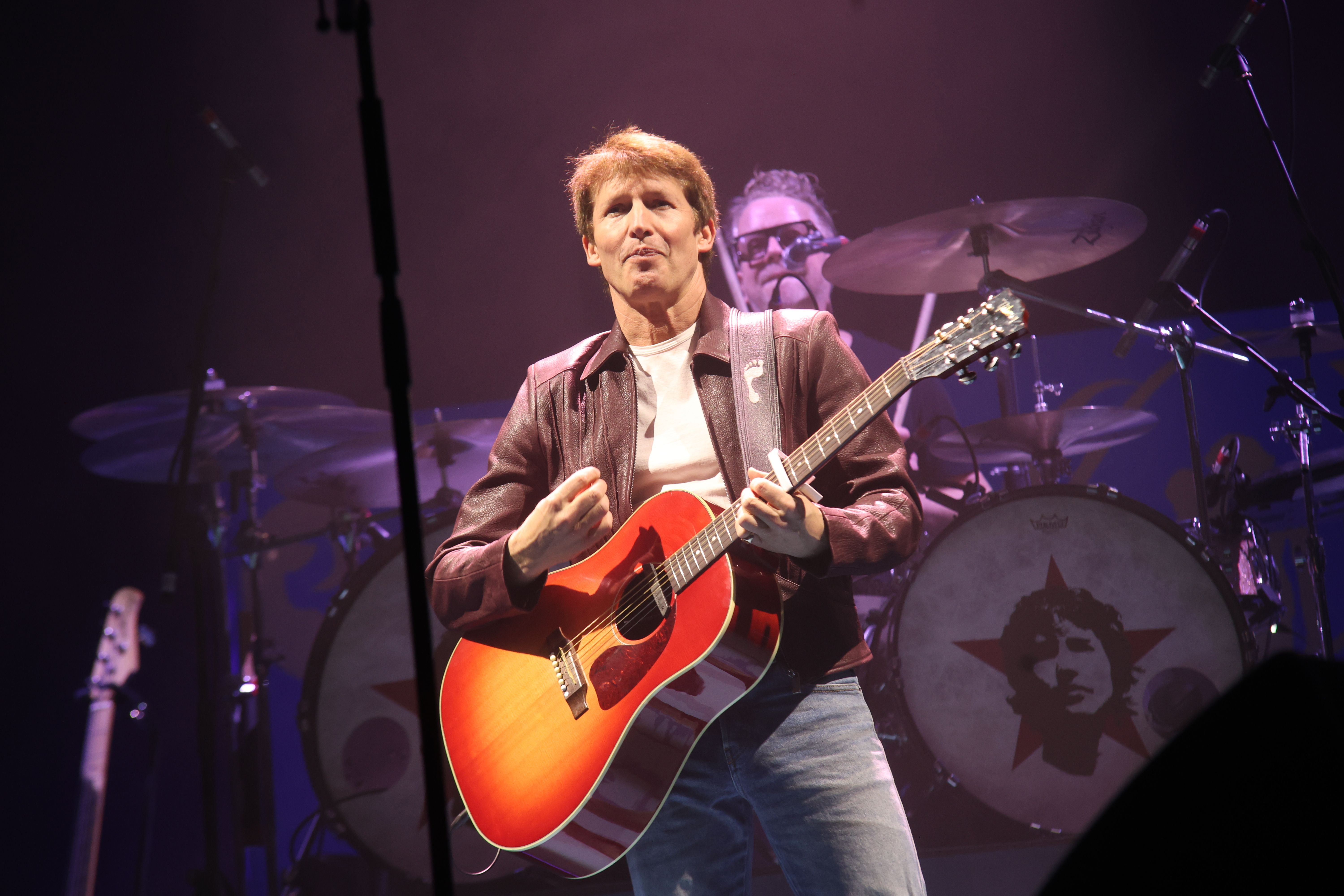 Mann spielt Gitarre auf der Bühne, im Hintergrund ein Schlagzeug mit Porträt auf der Trommel.