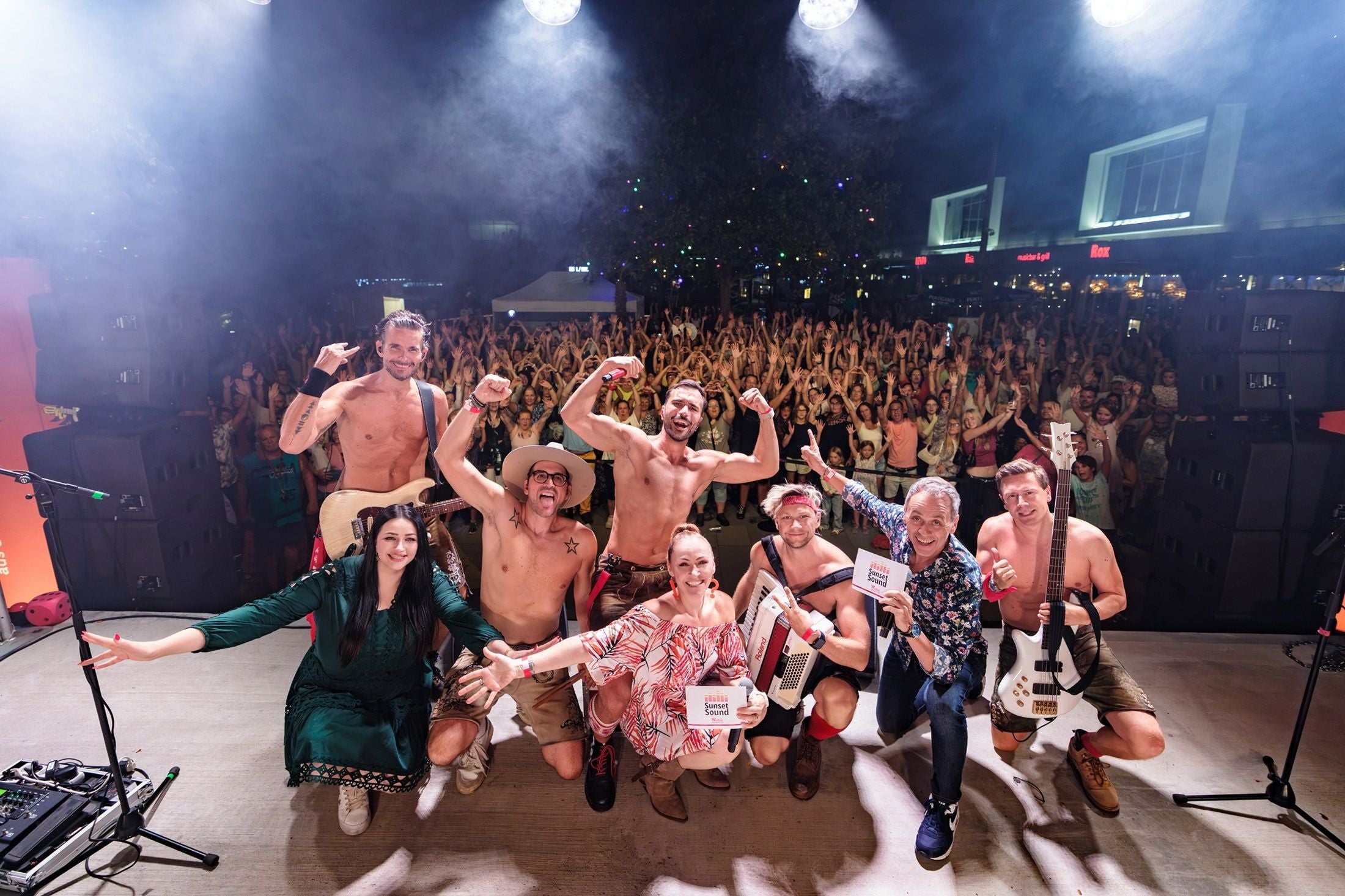 Band und Moderatoren posieren auf der Bühne vor jubelndem Publikum bei Sunset Sound 2026 Open-Air-Konzert.