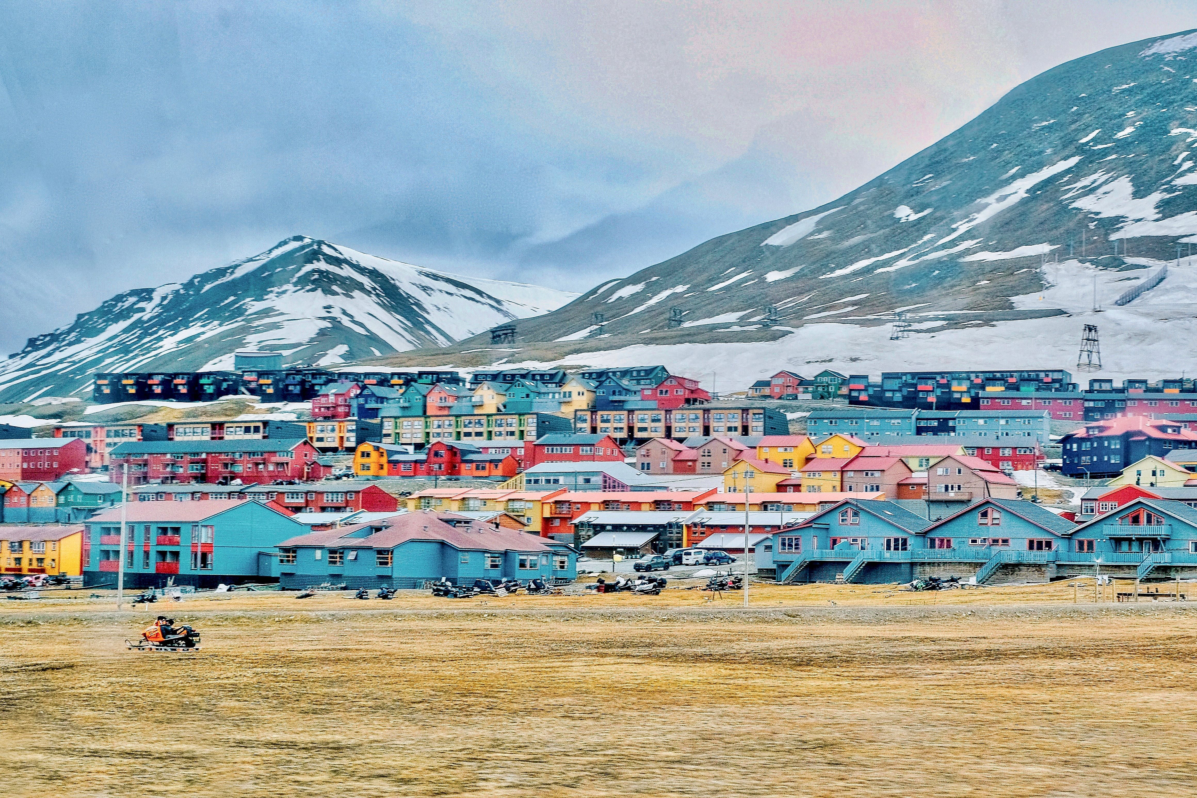 Bunte Häuser in Longyearbyen vor schneebedeckten Bergen, mit vielen Schneemobilen im Vordergrund.