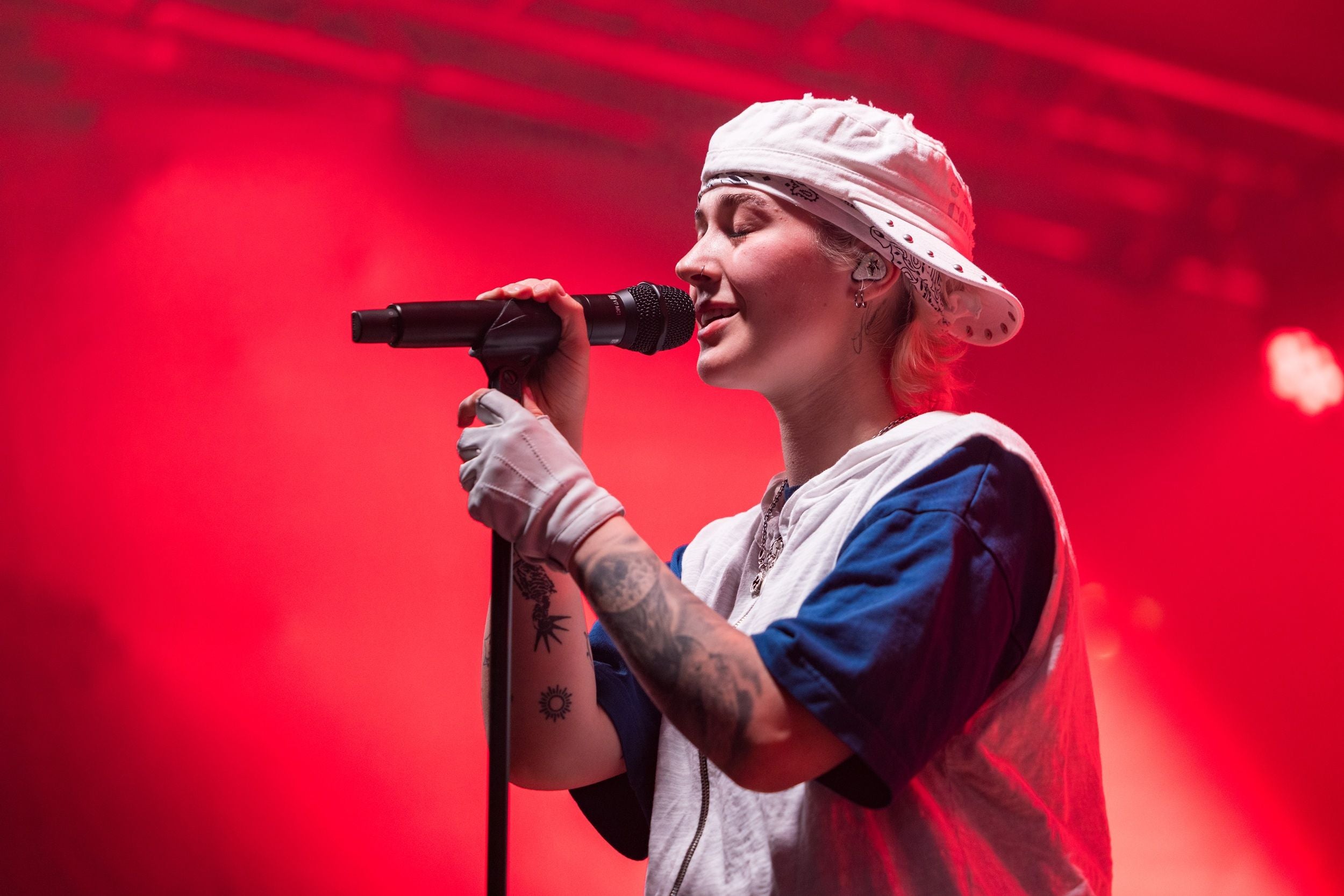 Sängerin mit Bandana und Tattoos singt auf der Bühne im roten Bühnenlicht.
