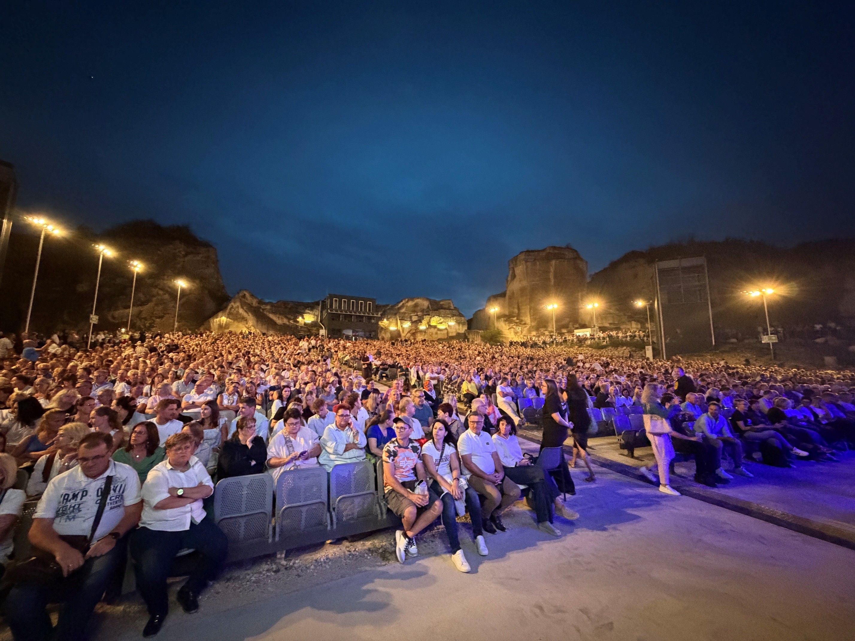 Großes Open-Air-Konzertpublikum am Abend vor Felsen und beleuchteter Bühne.