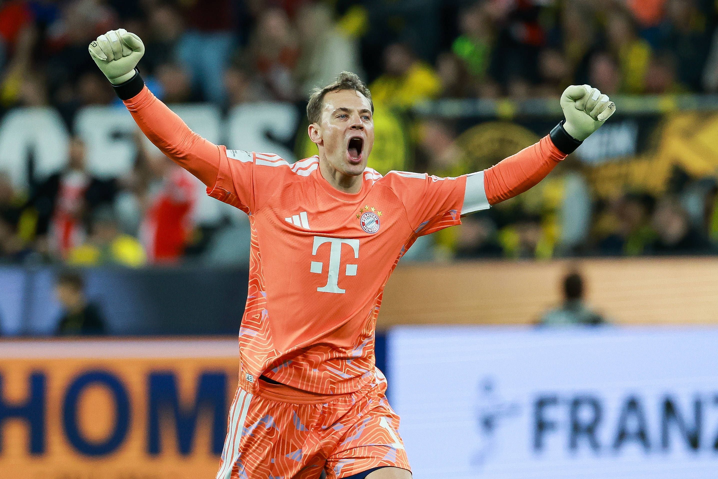 Torwart im orangefarbenen Trikot jubelt mit erhobenen Armen bei einem Fußballspiel im Stadion.