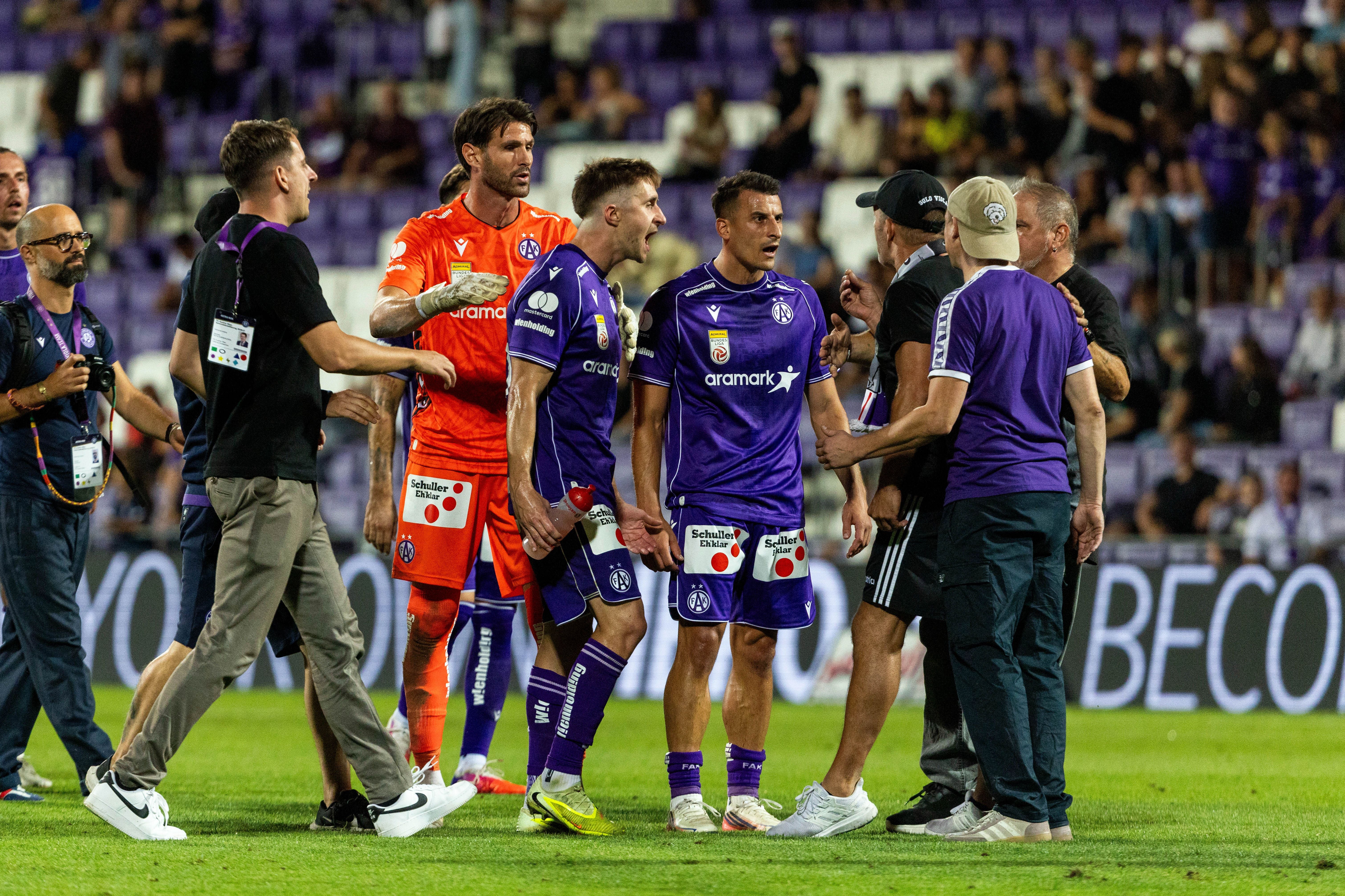 Fußballspieler und Betreuer von Austria Wien diskutieren emotional auf dem Spielfeld.