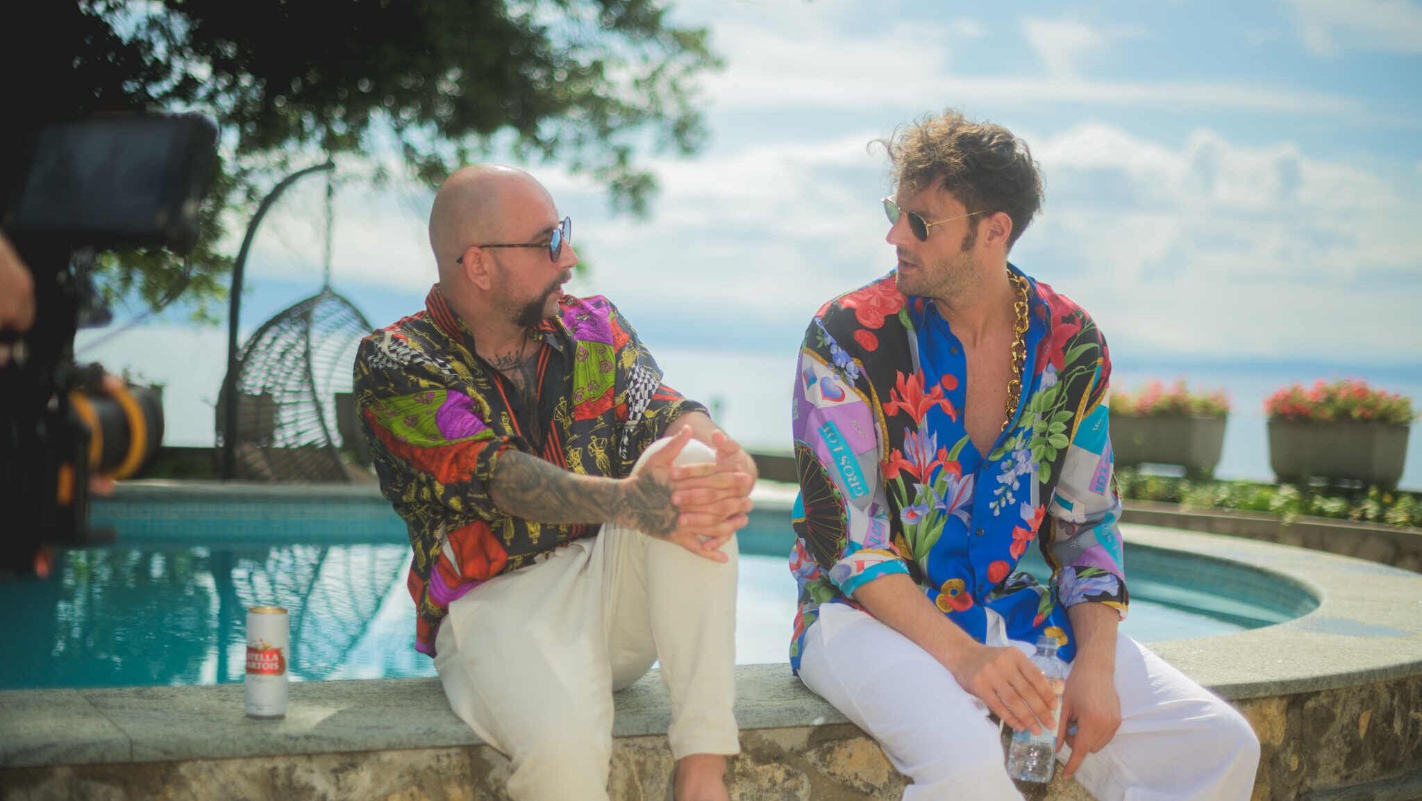 Zwei Männer in bunten Hemden sitzen am Pool und unterhalten sich entspannt.