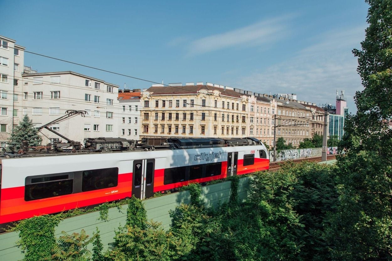Ein ÖBB Cityjet-Zug fährt auf der Stammstrecke durch eine Stadt mit historischen Gebäuden.