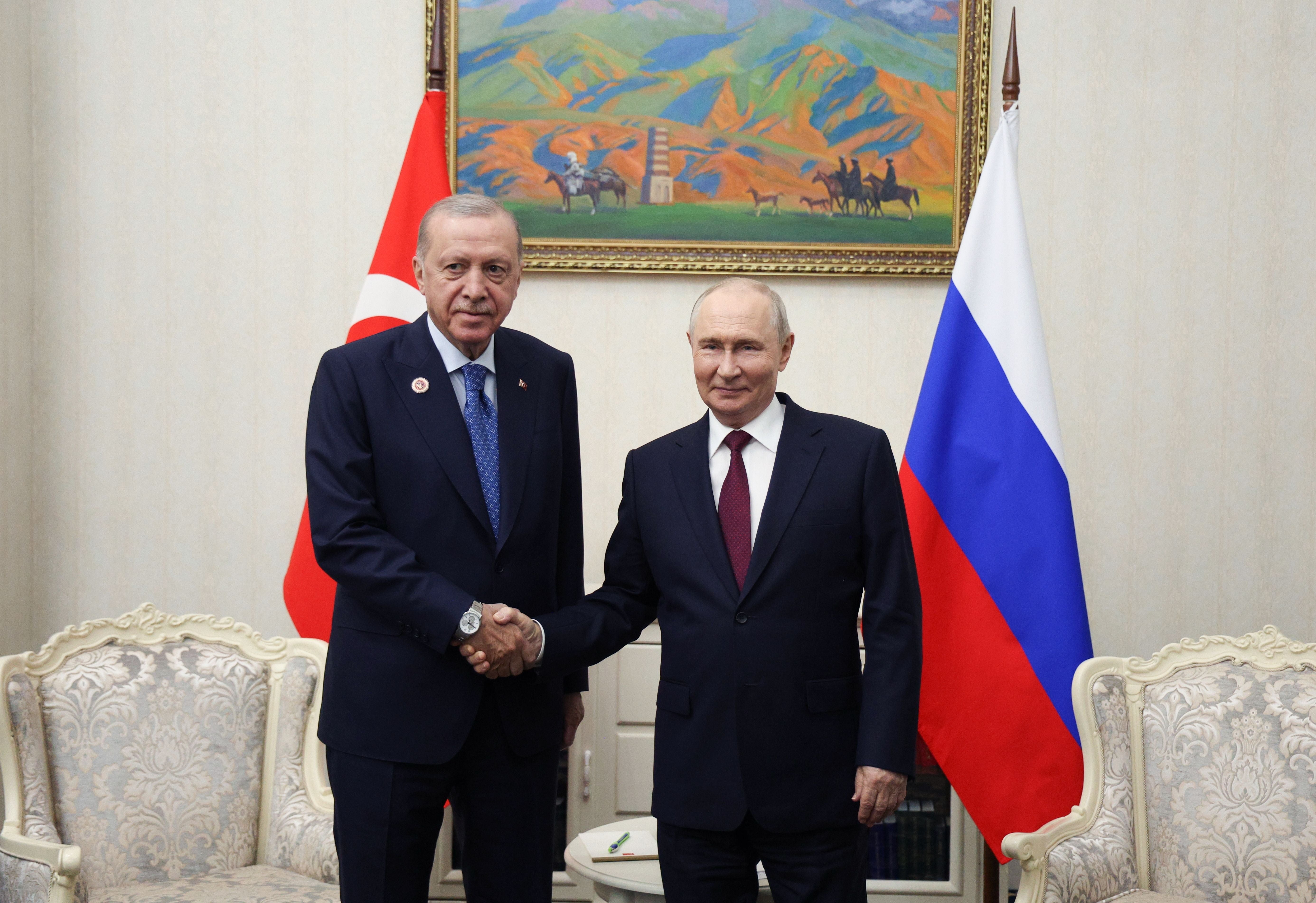 Zwei Männer im Anzug schütteln sich vor türkischer und russischer Flagge die Hand.
