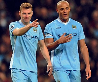 Edin Dzeko zeigt im hellblauen Manchester-City-Trikot mit dem Finger nach vorne, während Vincent Kompany lächelnd neben ihm steht.