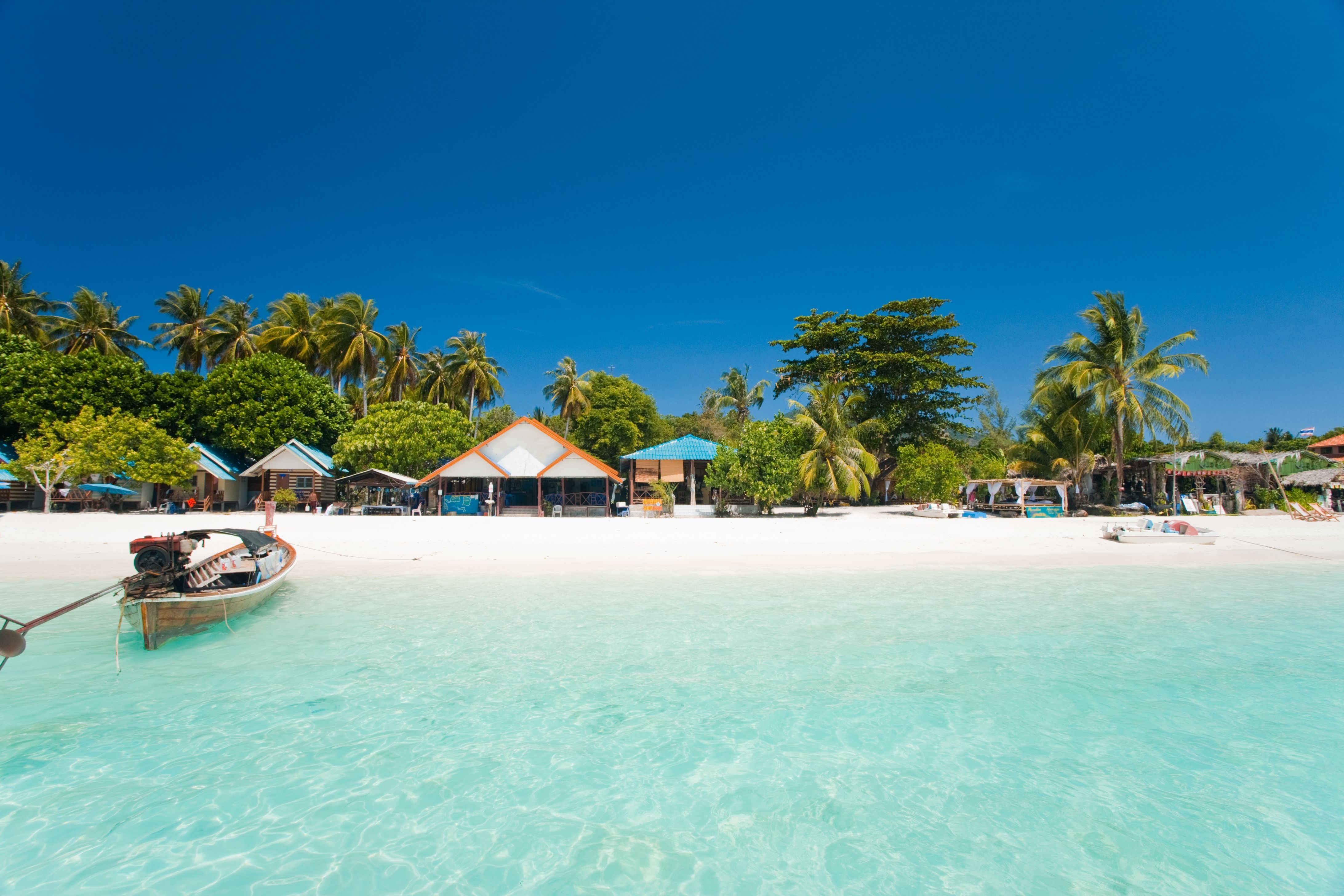 Weißer Sandstrand mit türkisfarbenem Wasser, Palmen und kleinen Hütten auf Koh Lipe, Thailand.
