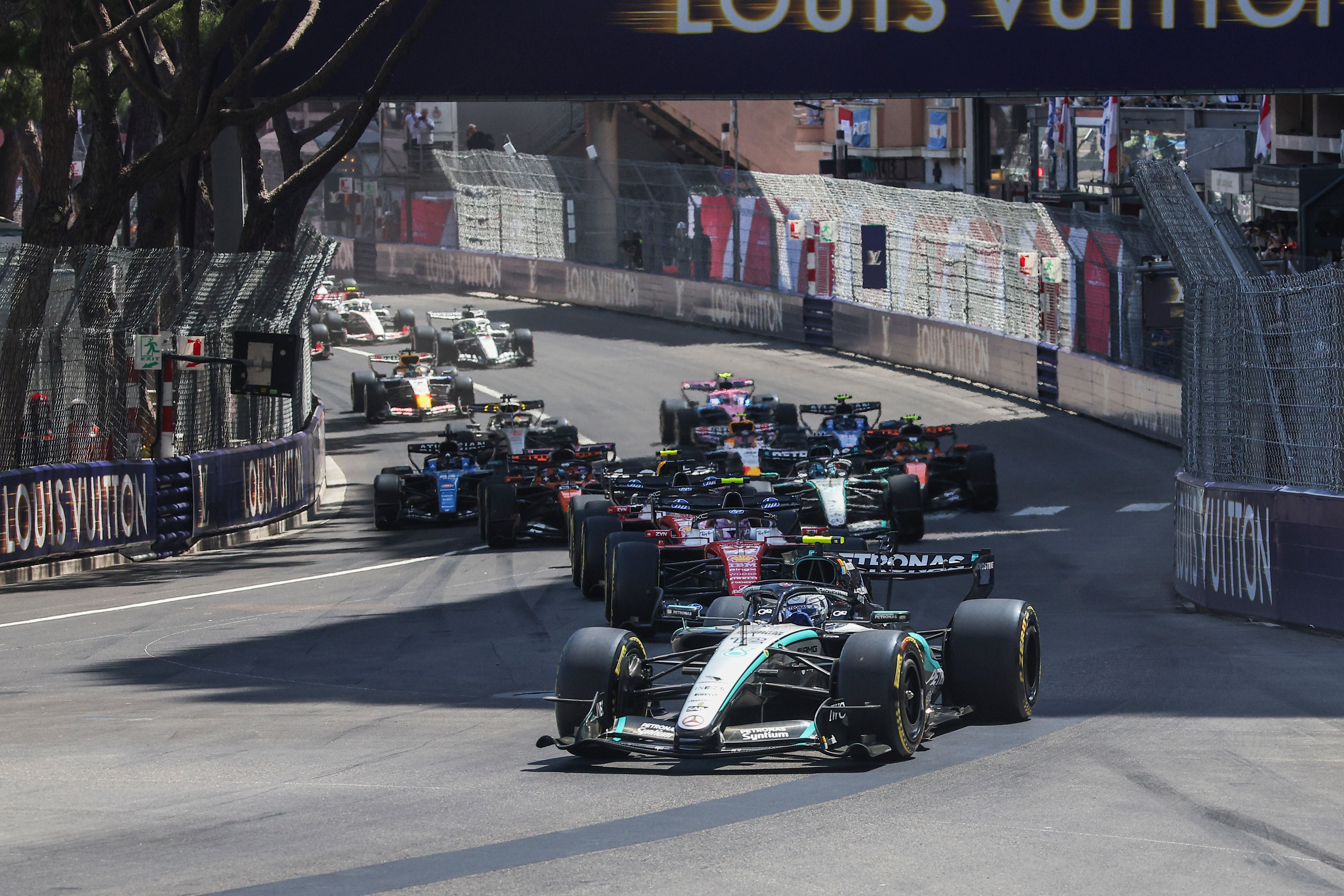 Mehrere Formel-1-Autos fahren beim Start des Monaco Grand Prix durch eine enge Straßenkurve.