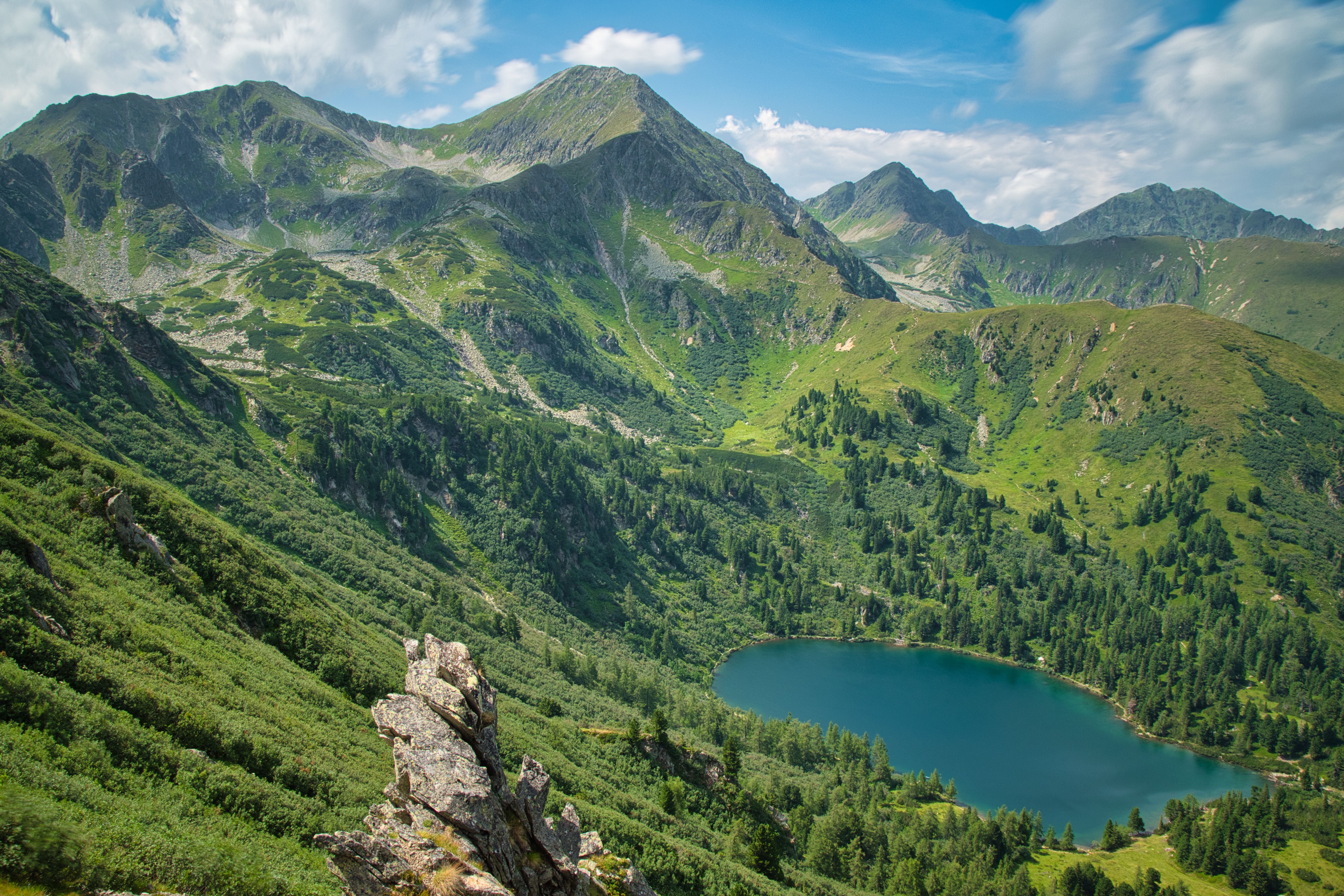 Grüner Berghang mit Scheiblsee und dem Großen Bösenstein im Hintergrund unter blauem Himmel.