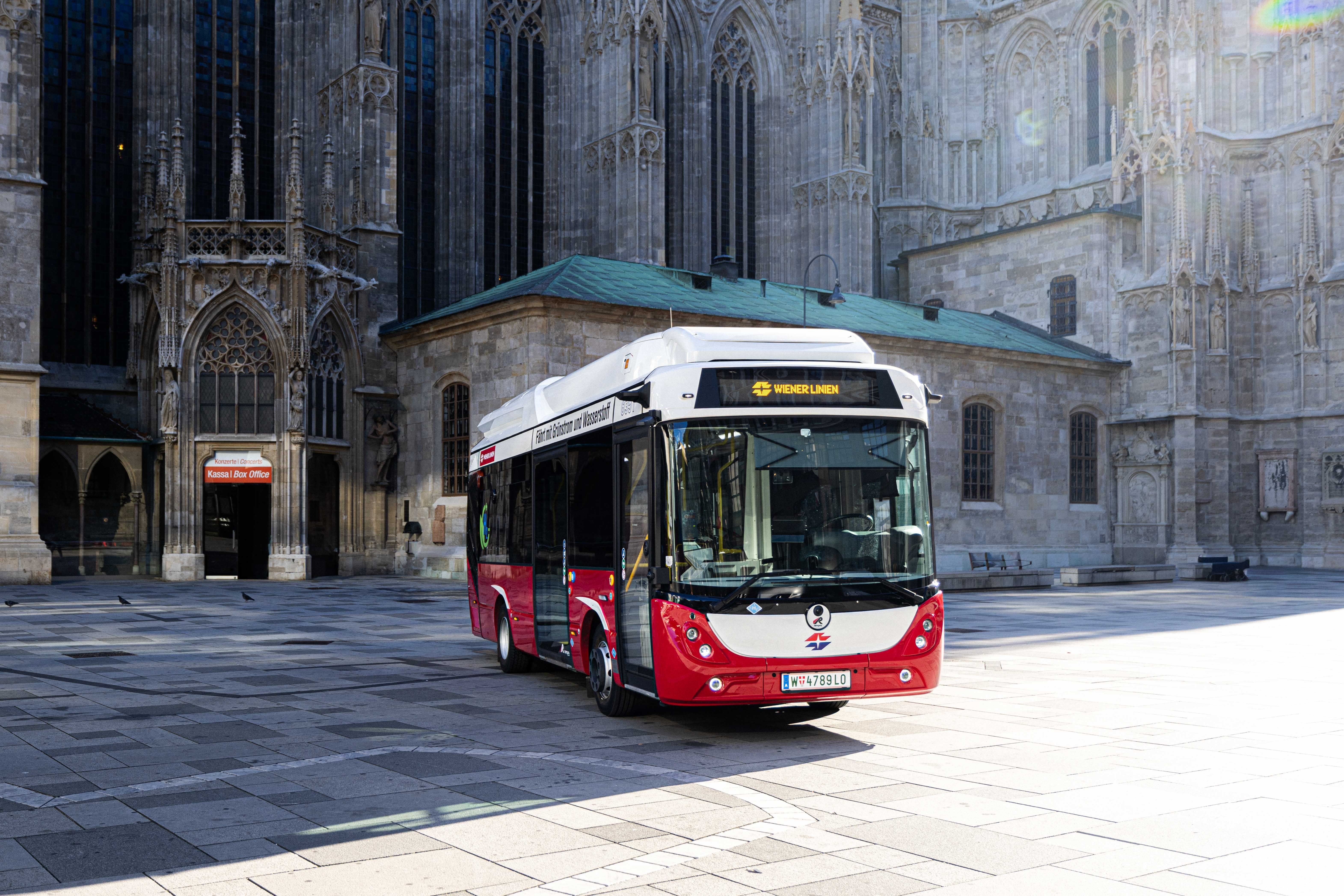 Ein moderner Wasserstoff-E-Bus der Wiener Linien steht vor einer historischen Kirche.