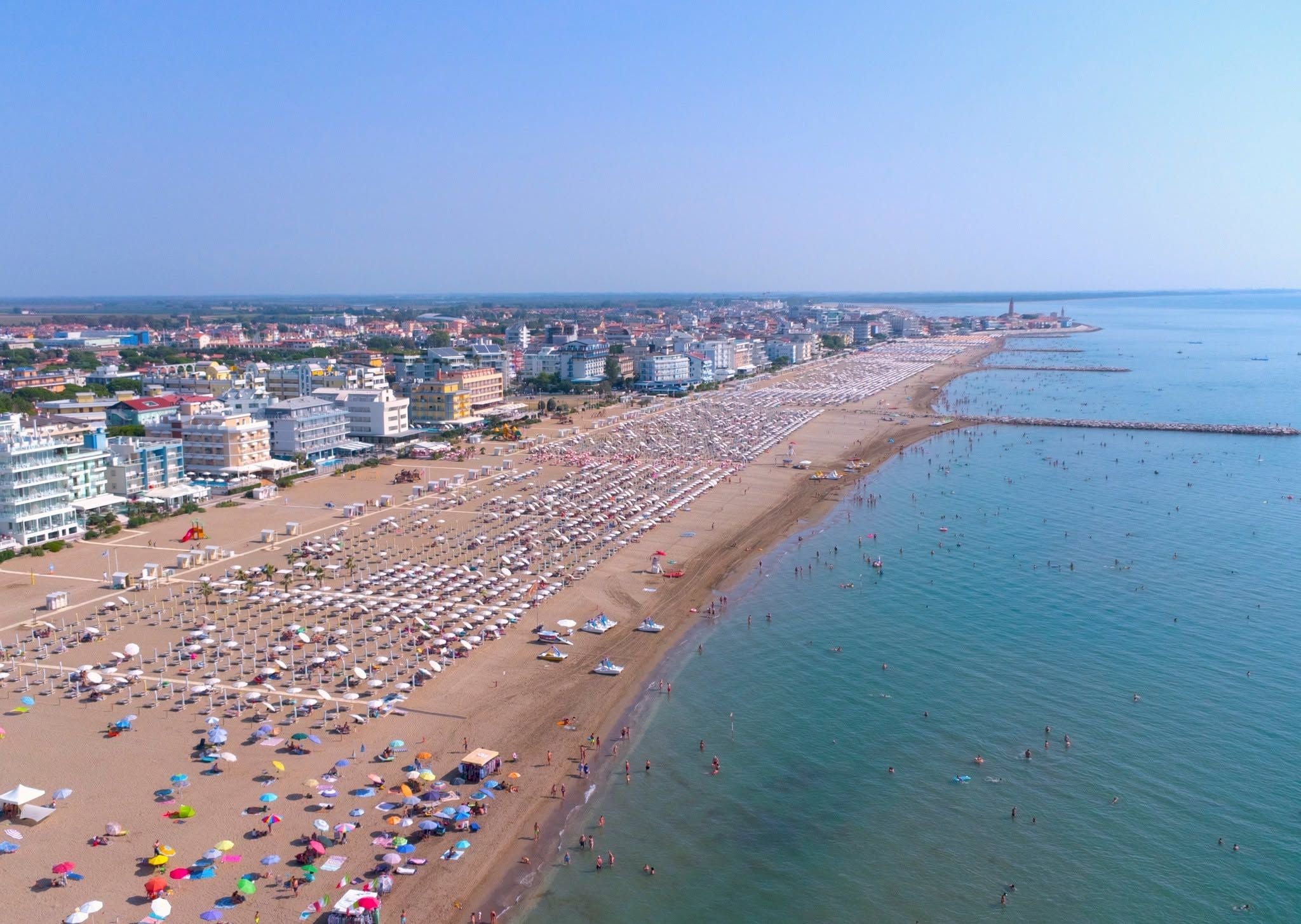 Langer Sandstrand mit Sonnenschirmen und vielen Badenden am Strand von Caorle, Italien.