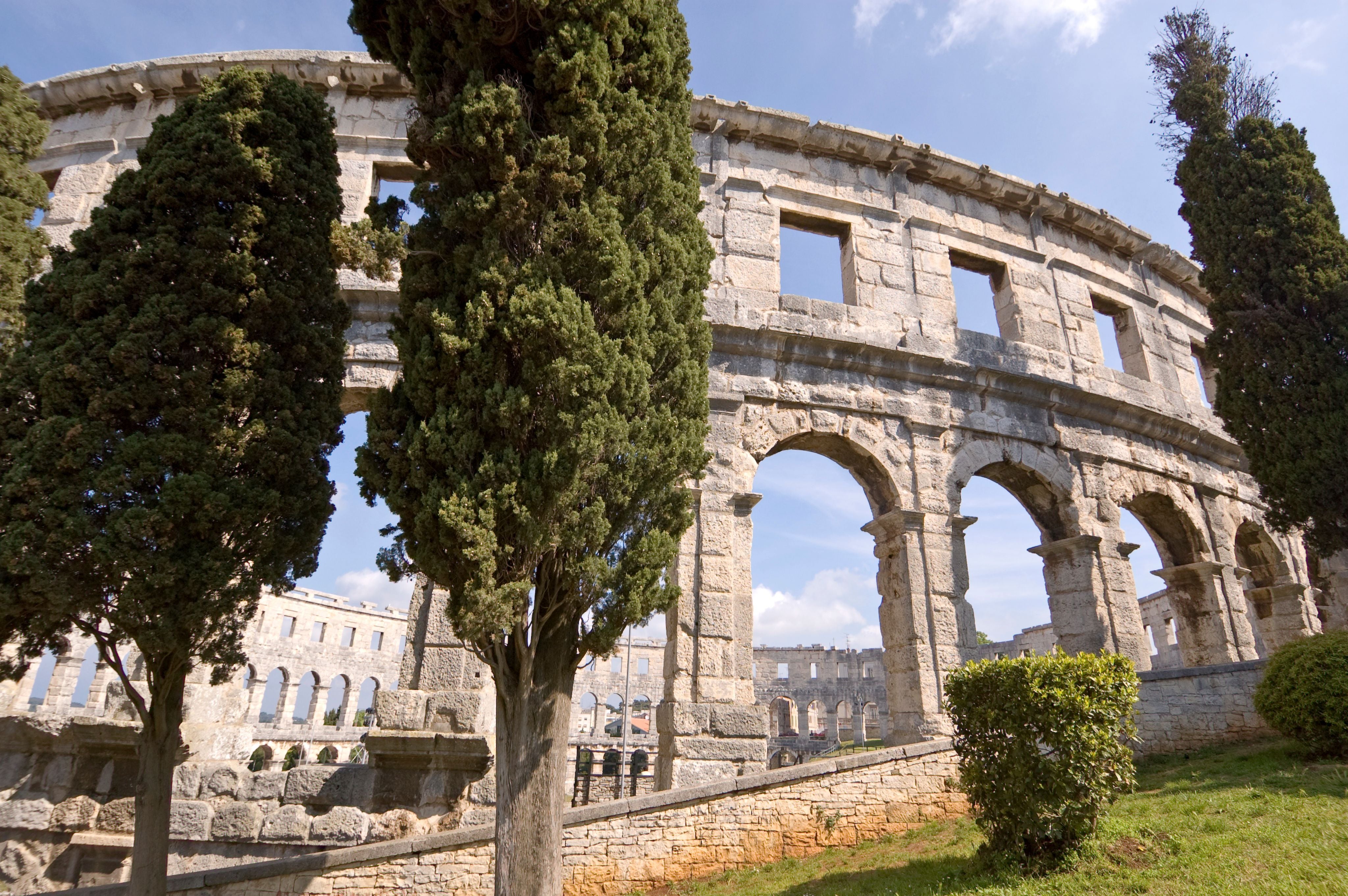 Römisches Amphitheater in Pula mit Bäumen im Vordergrund und blauem Himmel.