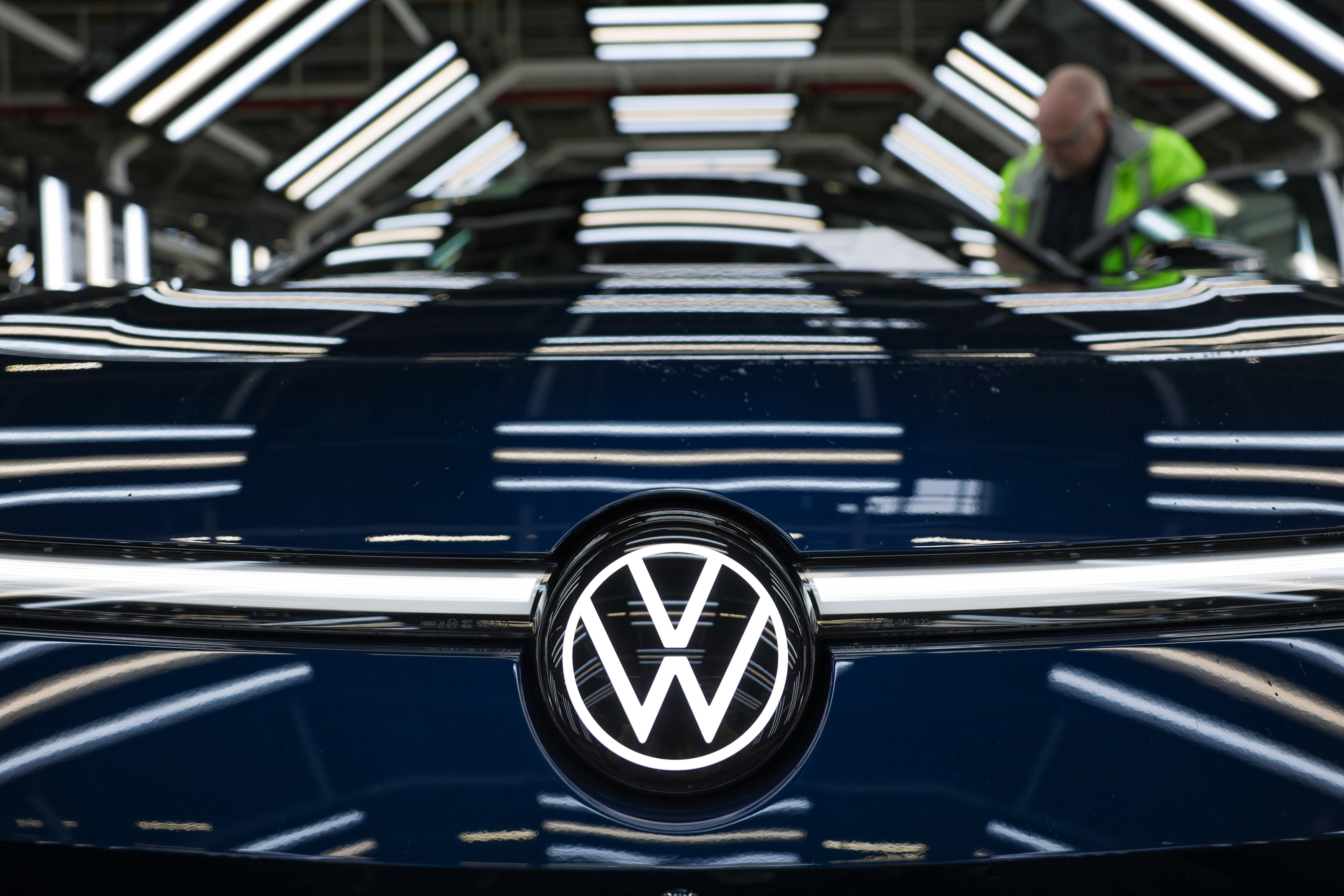 VW-Logo auf der Motorhaube eines Autos in einer beleuchteten Fabrikhalle.