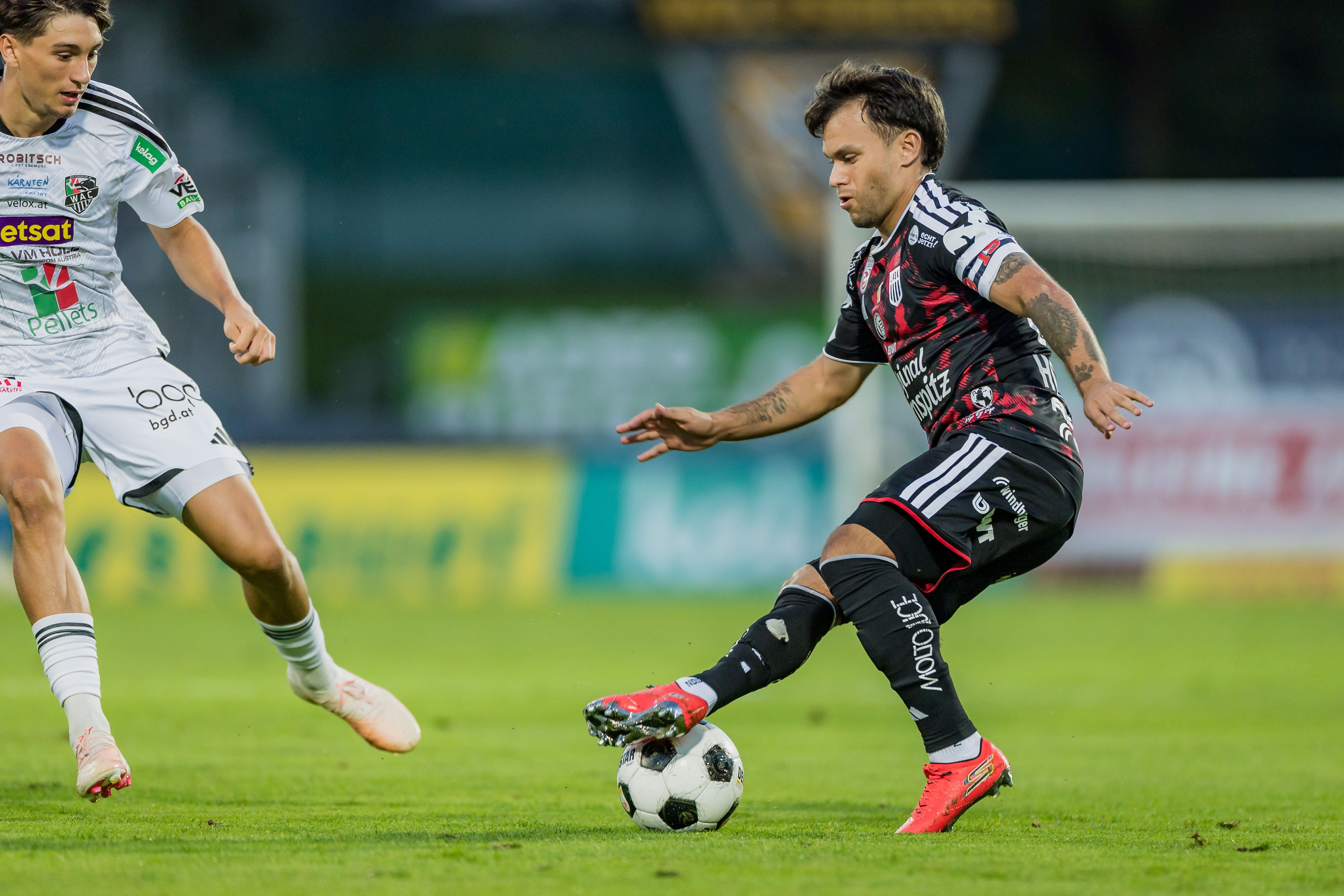 LASK-Kapitän Sascha Horvath führt im schwarz-rot gestreiften Trikot den Ball am Fuß und zieht an einem Gegenspieler vorbei.