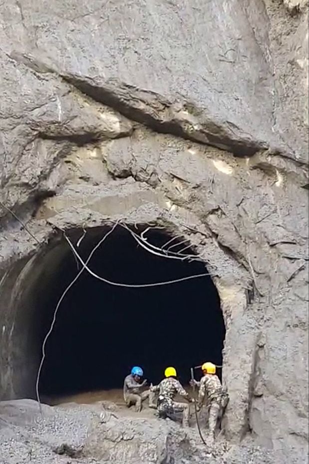 Drei Rettungskräfte mit Helmen retten eine Person am Eingang eines Tunnels in einer Felswand.