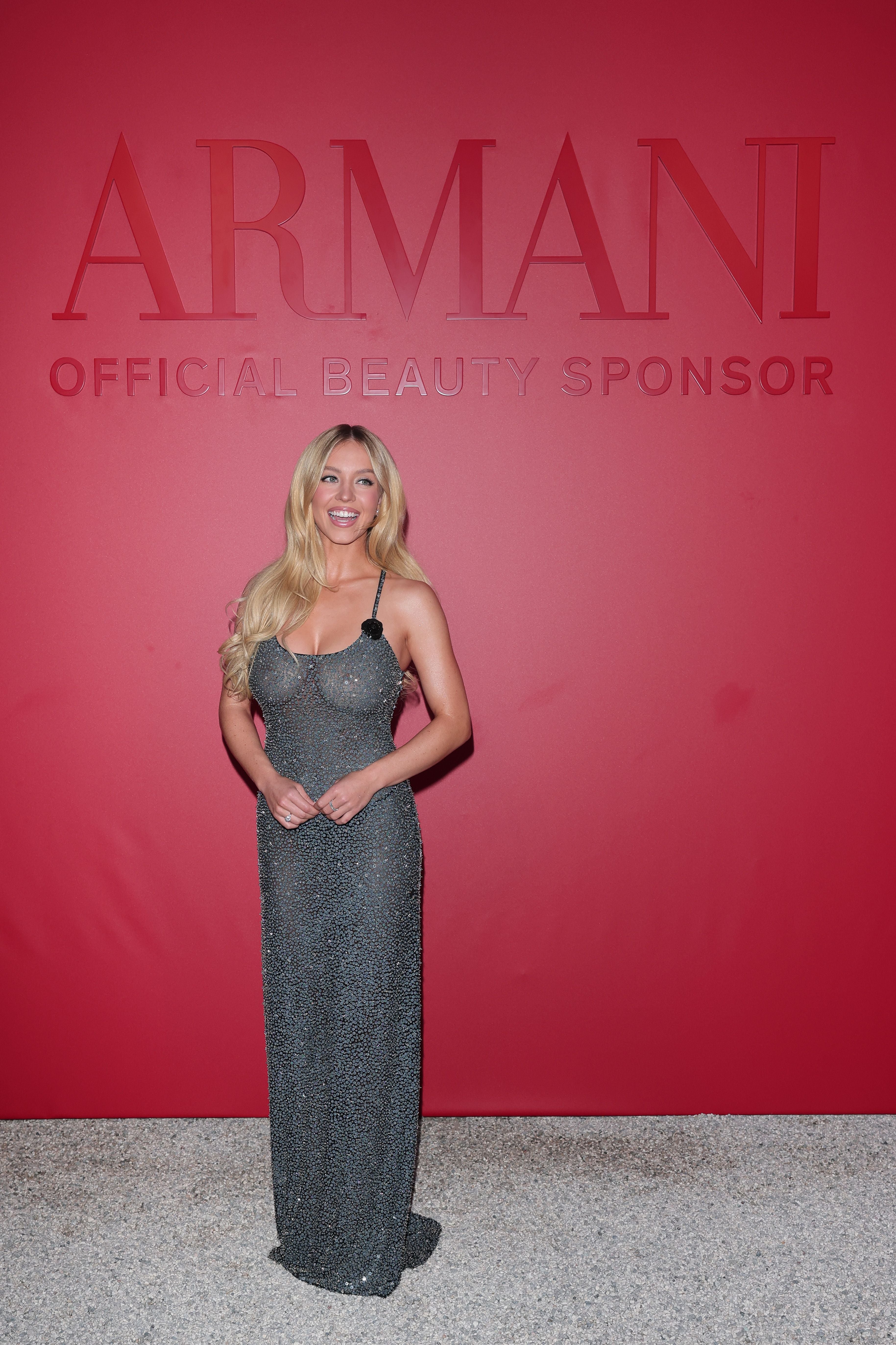 Frau im glitzernden Abendkleid posiert vor roter Armani-Beauty-Wand.