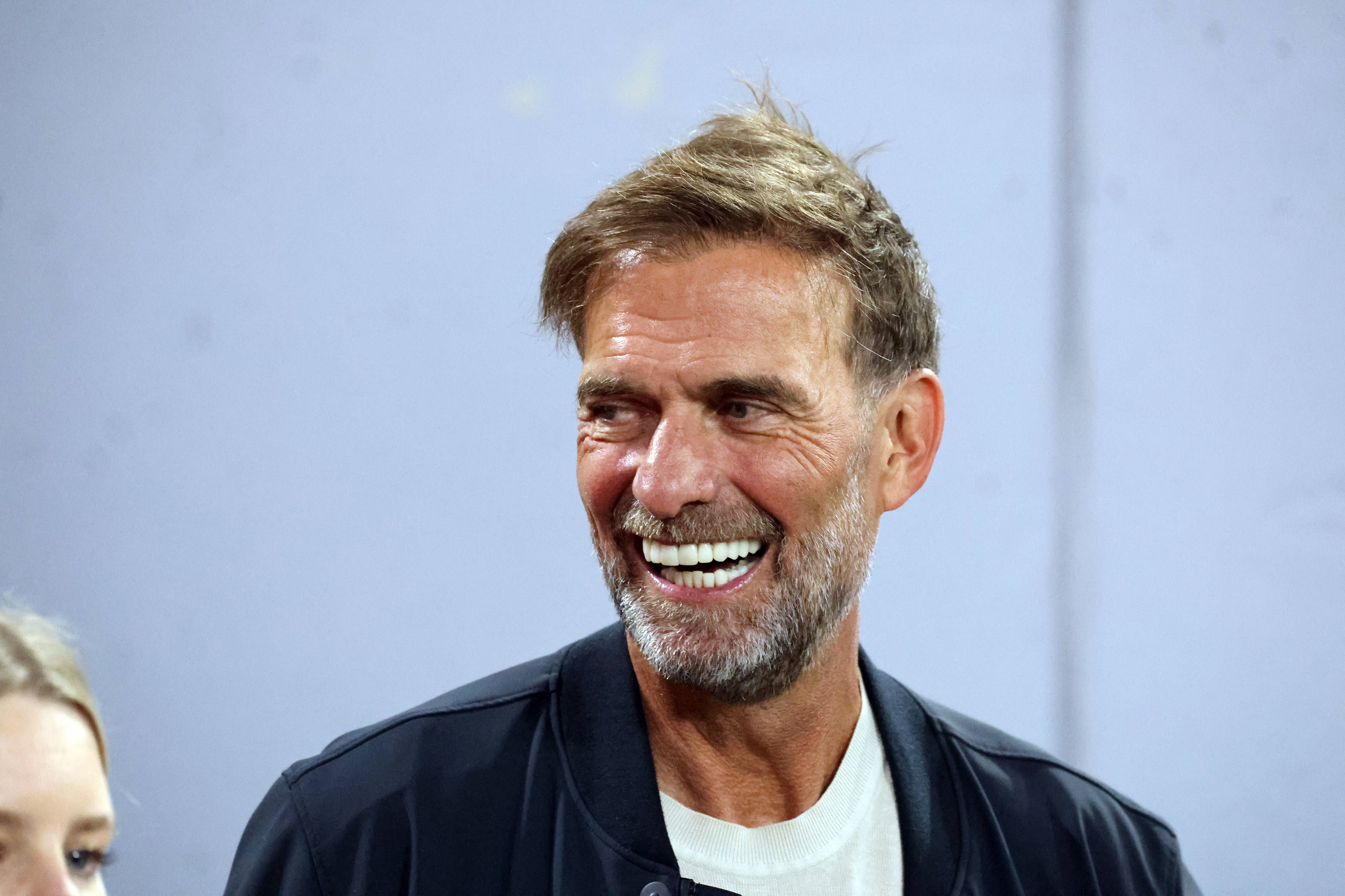Ein Mann mit Bart und kurzen Haaren lächelt vor grauem Hintergrund in die Kamera.